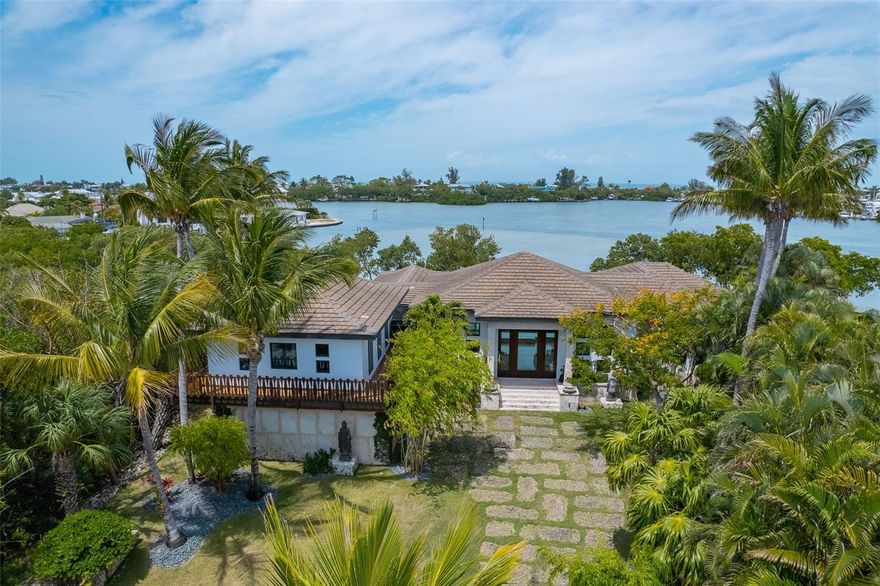 Located in the only GATED COMMUNITY on Anna Maria Island, this custom built residence is one of only eight homes on the private drive. Unparalleled privacy and worldly influences captivate a Zen-like atmosphere throughout this Balinese-inspired island home overlooking endless views of Bimini Bay. Built by Mason Martin Builders, exotic finishes adorn every space creating harmony between natural elements that accentuate exceptional craftsmanship and unique beauty. Balinese sculptures of volcanic ash greet you at the entry framing quarried coral stone pavers from the Florida Keys. A breathtaking sunken living room is equal parts stunning and comfortable, where a Koi pond boundaries the room and a wall of glass presents the incredible 160 feet of waterfront. A dream for entertaining, the living room is open to the outdoor living area and the kitchen, which boasts Wolf and SubZero appliances, beautiful sustainable African Sapele wood cabinetry, and luxurious soapstone countertops and fossil stone backsplash. Limestone floors throughout the interior and Triarch textured walls that have been imbedded with mica add to the organic feel of the home. Open the 32’ wide sliders to enhance and extend the gathering and dining spaces onto the private covered lanai with topless impact glass rails and heated infinity-edge saltwater pool. The epitome of serenity is found in the master suite featuring expansive glass for morning sunrise views and an en-suite bath showcasing a 2,500-lb soaking tub made from a hollowed-out boulder imported from Bali. A 10,000 lb boat lift has been newly installed on the separately deeded boat slip located at the end of the private drive, keeping your boat close while maintaining unobstructed views from the residence. A pristine location on Anna Maria Island, this home appreciates and takes full advantage of its oasis-like setting for a life of true bliss. Offered TURNKEY FURNISHED.