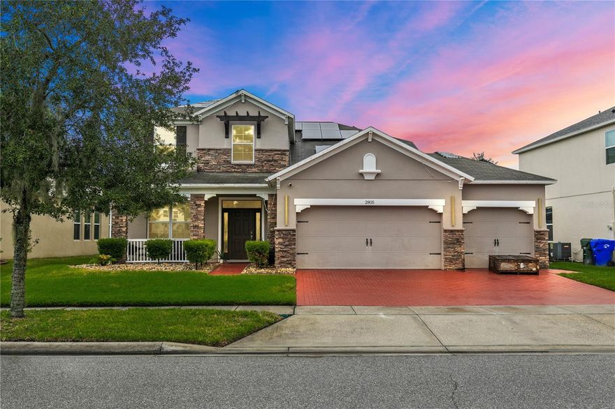 Welcome to this stunning move-in-ready home where thoughtful design, premium upgrades, and energy efficiency come together in perfect harmony. This beautifully maintained home offers the perfect balance of luxury, comfort, and convenience. From first glance, curb appeal impresses with a stone-accented front elevation, well-maintained landscaping, and a striking red brick walkway leading to a covered front porch. Step inside to a bright, airy foyer featuring polished porcelain tile, clean architectural lines, and a sleek glass-panel staircase setting the stage for the refined interior that follows. The open-concept main level is both stylish and highly functional. The family room is anchored by a custom entertainment wall with textured paneling, LED accent lighting, and a floating media console, an ideal setting for relaxed nights or elegant entertaining. Crown molding, recessed lighting, and a soft neutral palette enhance the elegant atmosphere, while wide visibility flow effortlessly into the dining area and kitchen. The kitchen is a true showpiece; a modern, sleek, and designed for both culinary performance and visual impact. High-gloss white cabinetry offers ample storage, white stunning quartz countertops with bold veining wrap around a dramatic waterfall island that doubles as a prep space and social hub. The waterfall island is anchored by a distinctive tile inlay, elevating the kitchen’s designer aesthetic., complemented by a sculptural LED pendant light overhead and ambient LED ceiling lighting throughout. Outfitted with premium stainless-steel appliances, the kitchen includes a Samsung French door smart refrigerator with digital display, double wall ovens, a smooth cooktop with a stylish range hood, and an integrated dishwasher. A continuous marble-look quartz backsplash ties the space together. Adjacent to the kitchen, the dining area is bathed in sunlight from sliding glass doors that lead directly to the backyard. Tucked beneath the staircase is a custom-designed bar nook complete with a stacked stone backsplash, glass shelving, recessed lighting, and a built-in beverage cooler, ideal for relaxing evenings or hosting guests. Nearby, a built-in display wall with individually lit niches offers a refined way to showcase art, collectibles, or personal décor. Upstairs, a spacious loft serves as a second living room or media lounge, featuring a textured accent wall, floating console, and contemporary lighting. Glass-panel railings maintain the home’s open feel while adding a modern edge.  The primary suite is located on the first floor, offering privacy and comfort. The ensuite bathroom includes a built-in closet system for efficient storage, along with updated fixtures and finishes for a clean, spa-like feel. Each bedroom features porcelain tile flooring, modern ceiling fans, and ample natural light. Bathrooms are tastefully updated, with three full baths and a convenient half-bath. Step outside to your private backyard retreat. A large, covered patio with wood-beam construction offers shaded comfort, while an expansive paver patio provides plenty of space for outdoor dining, lounging, or entertaining. A curved paver walkway leads past dual HVAC units and the solar energy system. Nestled just minutes from The Loop—a vibrant open-air shopping and entertainment destination, movie theaters, 20 minutes from Orlando’s world-famous theme parks and the Orlando International Airport. Schedule your private showing today!