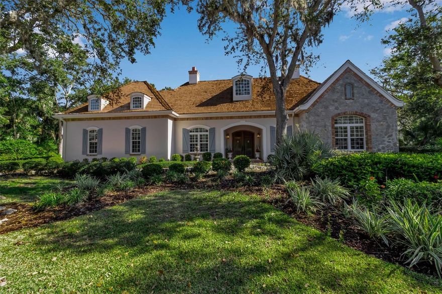 Although built in the 20th century, this home looks as authentic as the French manor house it was modeled after. The façade features a soft, light-colored stucco exterior accented by rustic stonework, creating a warm and inviting presence. Gracefully arched windows and classic dormers enhance the wooden shingle roof, which is crowned by two stately chimneys that add to the home's old-world charm. A gently curved brick-bordered walkway leads through a beautifully landscaped front yard, where manicured shrubs and vibrant flowering plants frame the path to the entrance. Bathed in sunlight under a clear blue sky, the entire scene feels like a serene countryside retreat—refined, welcoming, and effortlessly picturesque. In the main house, you’ll find high ceilings throughout, two bathrooms, three bedrooms, a formal dining room, and a large, dedicated office.  Separate from the main home is a large, one-bedroom casita with a vaulted ceiling, full bath, kitchenette, and room for a workspace.  The huge, fully-screened, 1,000 SF courtyard is beautiful with a vaulted pool cage, pool with built-in waterfall and a spa, and both sunny and shady areas perfect for morning coffee, lunch, or evening cocktails.  This home has everything to serve your needs, including those of multigenerational living and visiting guests. Step inside this courtyard style home and you will be greeted by a lovingly maintained, spacious, open floor plan interior. The high ceilings, skylights, and doors surrounding the courtyard ensure that every inch of the home is filled with light. The kitchen features a wide expanse of countertops including two sinks, a range with an ultra-quiet external fan range hood, and a dishwasher.  Surrounded by maple cabinetry and including a built-in microwave and refrigerator, this space will bring the joy of cooking to a chef of any level. The master suite is huge and features two walk-in closets, and an incredible bathroom with clerestory windows, dual sinks in the main area of the bathroom and one in the water closet, a jetted tub and a separate walk-in shower. The two guest bedrooms within the main part of the house are good sized, and there is a large laundry room with a utility sink and new washer and dryer.  Add to this all the practical features of A NEWER ROOF, IMPACT EXTERIOR FACING WINDOWS, RECENTLY REDONE POOL SURFACE AND EQUPIMENT, AND A 2 CAR GARAGE WITH TONS OF STORAGE SPACE, and you have everything you need to live an incredible lifestyle in The Oaks Bayside. Membership in The Oaks Club, Sarasota’s premier golf and country club, is mandatory with homeownership.