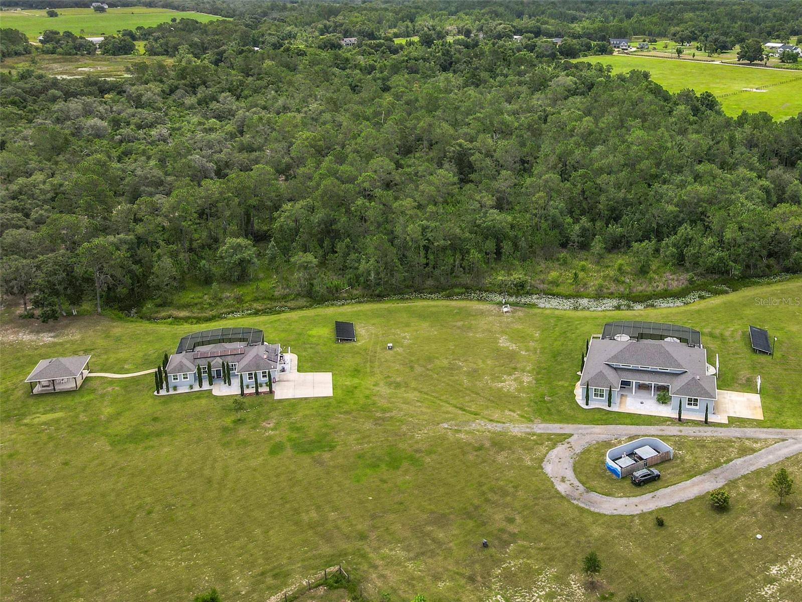 Rare 30-Acre Multifamily Compound featuring Nature, Luxury, and Expansion All in One! Welcome to a truly one of a kind park like estate with two beautifully appointed single-family homes, each with a solar heated lap pool! Totaling 5 bedrooms and 7 bathrooms this property has curated landscapes, and endless potential for expansion or enjoyment. Gated and private, this exceptional property offers the perfect blend of natural beauty, luxury amenities, and functional versatility - ideal for multigenerational living, private retreats, events, or future development. A top of line Leaf water filtration system enhance safety and comfort. With three wells(including two for irrigation), three fully paid-off solar panels (two for the heated saltwater lap pools and one for the guest house), and the use of non-toxic, natural fertilizers throughout the grounds, the estate delivers sustainable living with a focus on wellness. Step outside and experience extraordinary natural beauty with 300 hand-selected trees valued at over $200K, a curated forest with a cleared walking path, and a serene creek meandering along the rear of the property—all creating a haven for deer, cranes, songbirds, and other wildlife. Towering bamboo ensures privacy and tranquility, while fruit trees including avocado, mango, lemon, lime, peach, and loquat offer seasonal abundance. Enjoy the outdoors with two elegant gazebos—one of which is fully equipped with electricity, a ceiling fan, and electronic blinds. There is also a Hawaiian-themed garden, and cleared land ideal for camping, events, or recreational use. Whether you’re hosting weddings, forest bathing experiences, or fireworks displays, this property is built for unforgettable moments. Inside the main house, discover unique chandeliers, plantation shutters on all bedroom windows, and scenic forest views from every window, creating a harmonious indoor-outdoor flow. Both homes are furnished with Serena & Lily, blending relaxed luxury with timeless elegance and furnishings that are available as an option for a turnkey lifestyle. The high end pool umbrellas for both homes are included with the sale. Other exceptional features include a dedicated shooting range and the zoning flexibility to build a third structure or barn, offering room to grow and evolve with your needs. This is more than a home—it's a multifamily sanctuary designed for those who value luxury, nature, privacy, and potential. A rare opportunity to own an estate that inspires, nourishes, and invites you to live fully!
