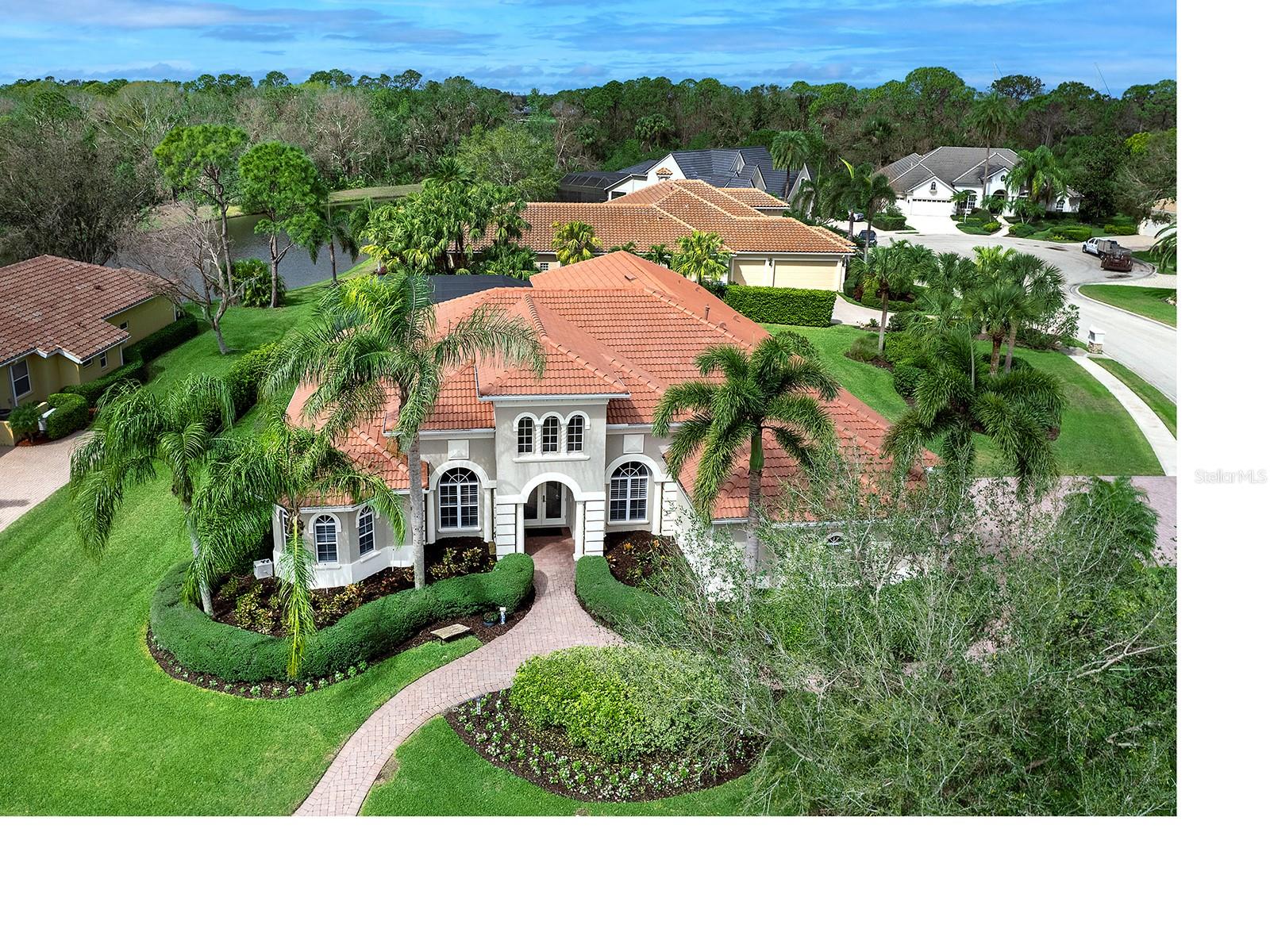 On a beautifully landscaped corner lot in esteemed Lakewood Ranch Country Club, this residence offers an exceptional blend of elegance, functionality and a serene lake view. New roof in December 2024. The home’s striking exterior features an oversized paver driveway with manicured hedges, landscaped islands, a side-load garage with windows and a stately entrance framed by two columns. The glass double doors open to a foyer with a custom-trimmed wall niche and tile floors with a decorative inlay, setting the tone for the refined interior. Designed for grand entertaining and comfortable everyday living, the formal dining room boasts a double tray ceiling with crown molding and plantation-shuttered windows, while the living room impresses with soaring ceilings, custom moldings, a gas fireplace flanked by built-ins, and 10-foot sliding doors that invite indoor/outdoor living. The office, enclosed by glass French doors, is adorned with crown molding, hardwood floors and a large window with plantation shutters. The kitchen is designed for culinary excellence with quartz countertops, a glass tile backsplash and soft-close cabinetry. A central island provides prep space, while the counter features plenty of seating. The breakfast area offers views of the lanai and lake through an aquarium window. High-end stainless-steel appliances complete the space. The adjacent family room is ideal for gathering, featuring a tray ceiling, a built-in entertainment center, and walls of sliders that lead to the lanai. The primary suite is a retreat accessed through an alcove entry with double doors and a wall niche. A double tray ceiling, bay windows, beadboard accents and private lanai access through a glass door creates a serene atmosphere. The expansive walk-in closet is thoughtfully designed. The recently updated primary bath showcases an oversized walk-in shower with beautiful tile and seamless glass, porcelain tile floors, a dual-sink vanity with quartz countertops and a linen closet with wood shelving. Two additional bedrooms, each with walk-in closets and large windows, are well-appointed. One is an en suite, and two share a full bath with a tub and shower. A full pool bath with a glass-enclosed shower and hallway linen closet is conveniently accessible. The bonus room offers pocketing sliders, a spacious wall closet, access to the en-suite pool bath and flexibility to serve as an additional bedroom. Designed for year-round enjoyment, the lanai is fully equipped with an outdoor kitchen, complete with a Sedona Lynx grill, Fire-Magic mini refrigerator, prep sink and weather-resistant cabinetry, and plenty of bar-height seating at granite countertop. The lanai’s Pro-Deck rubber flooring is eco-friendly, UV-resistant and anti-fungal, ensuring durability and comfort. A gas-heated pool and spa, two large, covered areas for dining and lounging, and lush landscaping enhance the tranquil ambiance with its breathtaking lake view. With the recent expansion to include a fourth golf course, Lakewood Ranch Golf and Country Club offers unmatched access to premier golfing. Residents can choose from a variety of membership options. Ideally just minutes from the UTC Mall, Waterside, Lakewood Ranch Main Street and downtown Sarasota, the home is also within easy reach of top-tier dining, shopping and the area’s renowned beaches. 7934 Royal Birkdale Circle is a stunning residence in one of Lakewood Ranch’s prestigious communities.