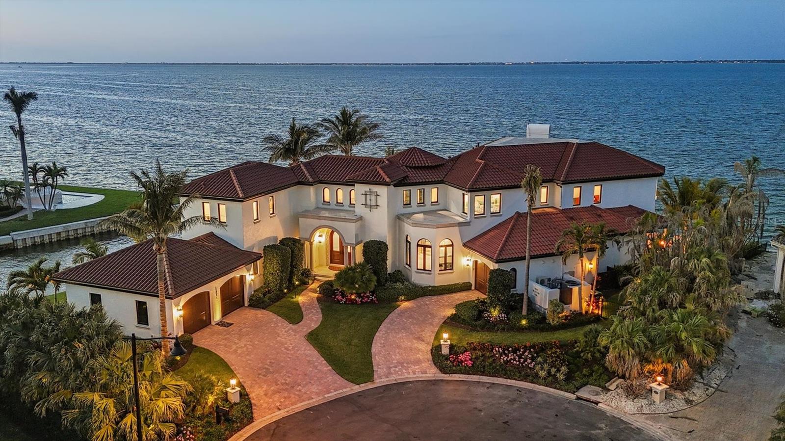 Under contract-accepting backup offers. A luxurious coastal retreat at the water’s edge on Longboat Key, 641 Ranger Lane captures the essence of relaxed waterfront luxury. Set on a rare .42-acre corner lot with over 270 feet of prime waterfrontage, this coastal estate offers four bedrooms, 5.5 baths and 7,033 square feet of refined living space. With sweeping views from nearly every room, this home lives as beautifully as it entertains. A dramatic foyer and staircase introduce the home and the craftsmanship throughout. Travertine floors and dark crown molding flow through the main living areas, and a two-stop elevator adds effortless access to all levels. The open-concept great room appeals with a sleek linear fireplace and walls of sliding glass doors that frame the water, blurring the boundary between indoors and out. The beautifully designed kitchen was created with function and flow in mind. Two oversized islands feature seating, dual wine coolers, ice makers and generous storage. The professional-grade Sub-Zero refrigerator, Wolf cooking suite, custom pantry with a built-in coffee station complete with pot filler and coffee pod drawer, and hidden outlets throughout speak to thoughtful luxury. Start your day with coffee in the window-lined breakfast area and end it hosting guests in the elegant dining room with designer wallpaper, a statement chandelier and room to entertain. Step outside to experience island living through a series of outdoor vignettes. A covered area with a wood ceiling and built-in wet bar sets the stage for alfresco dining with coastal breezes. The infinity-edge pool appears to spill seamlessly into the water beyond. Nearby, a hammock sways between two coconut palms, while a fully equipped outdoor kitchen leads to a sunken fire pit lounge, near the seawall for unobstructed views of the bay. With a concrete seawall and ample room for a new custom dock and lift (waiting for installation date), the property is primed for water enthusiasts. The first floor also offers a bonus space— a bunk room—with soaring ceilings, coastal design and sliders to the pool deck. A guest suite features a walk-in closet, designer wallpaper and an en-suite bath. The adjacent laundry room includes quartz countertops, Whirlpool appliances, and generous storage. Upstairs, the primary wing is a sanctuary with double tray ceilings, a linear fireplace, and two private balconies with incredible views. The spa-inspired bath is clad in marble and features a soaking tub, a smart temperature-controlled shower with waterfall fixtures, a makeup vanity and a Toto commode. Dual walk-in closets are thoughtfully designed for form and function. A private office with a wood-paneled ceiling, tile flooring, and balcony access provides a peaceful workspace or retreat with serene water views. Hallways lined with windows of vistas lead to private guest suites with spa-like baths, balconies and water views. A second laundry room and full bath add everyday convenience. Experience the ultimate island lifestyle where coastal sophistication meets everyday serenity. In Longboat Key’s Country Club Shores community with deeded beach access and proximity to golf, tennis and boating, this home offers easy access to The Longboat Key Club, The St. Regis, St. Armands Circle and downtown Sarasota. Recently named one of Forbes Travel Guide’s Top 12 Destinations for 2025, Longboat Key is where waterfront living comes to life.