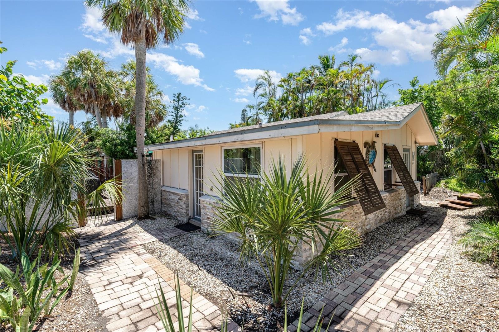 Step back in time and experience the “Old Florida Lifestyle” in the heart of Longboat Key’s historic Longbeach Village! Tucked away on the northernmost end of the island, this rare property features two charming Key West–style beach cottages on one lot, surrounded by lush tropical landscaping for a truly private island retreat.
The main updated cottage offers a light-filled, open floor plan with 2 bedrooms, 2 bathrooms, a den, laundry room, and spacious living area. The kitchen was tastefully updated in 2021 with quartz countertops, hardwood cabinets, and newer appliances, complete with a breakfast bar for casual dining. Open the windows and let the coastal breeze fill your home, or step outside to the wooden deck and tiki bar—perfect for entertaining and enjoying evenings listening to the nearby Gulf waves.
Across the wooden overpass sits the guest cottage, a cozy retreat with 1 bedroom, 1 bathroom, full kitchen, living space, and a private porch. It even has its own access via the private alleyway, making it ideal for visitors or rental potential.
Additional updates include Hardie board siding (2021), appliances (2021), quartz countertops (2021), cabinets (2021), and A/C (2017), ensuring modern comfort while maintaining that laid-back island vibe.
With no HOA or deed restrictions, this property offers flexibility for personal use or investment. Best of all, it’s just steps from both the beach and the bay—enjoy Whitney Beach, two fishing docks, the community boat/kayak launch, and popular dining at Mar Vista and Shore.