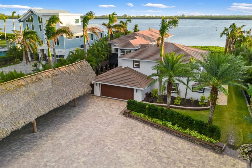 Huge $1,500,000 price reduction!!! This is a great opportunity. Welcome to this slice of paradise that is situated on nearly one acre with full bay views and beyond. Just a 10-minute boat ride to the Gulf of Mexico. A property that did not get any flooding from the recent hurricanes. As you enter through the wrought iron gates, you will work your way down a winding paver driveway adorned with lush royal palm trees, arecas, and grand oaks. The main entrance has a beautiful fountain, and a 7-car covered newly built tiki parking area. Upon entering this stunning home, your eyes take you right to the bay views that adorn this 101-foot-wide lot. Lounge in the oversized living area or make your way to the custom kitchen complete with 2 eating areas that allow you to take in all the views of the bay. It is a perfect set-up for entertaining around the kitchen island. There is a 48” Wolf gas stove, 48” Sub-Zero fridge, coffee maker, wine fridge, two drink fridges, and the list goes on. The counters are a stunning array of colors that enrich the dark cabinets. Lots of sliders allow you easy access to the custom outdoor kitchen. Moving through the house, you come to a separate dining room with another complete kitchen that can be used for parties or for a family member living at home. A private drinking area is a relaxing spot to stop after a busy day. There is an additional den/office off the second kitchen and comes complete with an en-suite bedroom and bath that can serve many functions. The wrought iron rails lead you up the stairs to 3 additional bedrooms and the owner's suite wing, which can also be accessed via an elevator in the main foyer area. The owner's suite is complete with two walk-in closets and a workplace in the larger closet. Enjoy a steam shower in the oversized shower or relax in your freestanding tub and take in the sunset. The owner's suite is laid out to take in the stunning sunsets. There is a mini kitchen that is complete with a wine fridge, dishwasher, fridge, and Wolf induction cooktop. Sliders take you out to a beautiful, updated deck and patio area with a spiral staircase that will take you down to the pool area and tiki hut on the water. Enjoy complete privacy by the oversized pool or sit down by the water on the paver deck area. Maybe you want to jump into your boat and go have dinner at a restaurant on the water or just head over to the beach. The sky is the limit with this property. There is also enough room to add an additional structure. Just recently appraised at $5.3 million. Make your appointment to see this beautiful home.
