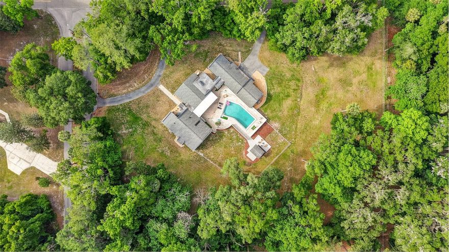 A Rare offering of Privacy, Scale, and Sophistication—this Jaw-Dropping, One-Of-A-Kind Estate has just debuted in Ocala and is truly a MUST SEE! $30,000 GIFT AT CLOSING! Tucked away on 2.59 acres of beautifully wooded land, this nearly 5,000 sf Pool Residence delivers the ultimate blend of refined living and peaceful seclusion with NO HOA, and the entire property fully fenced for added privacy and security. From the moment you arrive, the sense of space is undeniable. Expansive grounds provide abundant room for all your toys while offering wide open land to enjoy, entertain, and create your own private retreat. Step inside to a welcoming foyer which opens into a thoughtfully curated layout that leads to a breathtaking central living space. The grand family room is nothing short of spectacular, showcasing Soaring Cathedral Ceilings with Exposed Wood Beams, Rich Tongue-and-Groove Planks, and a warm, Elevated “Luxury Lodge” Ambiance. A custom bar anchors the space, perfect for entertaining, while oversized sliders seamlessly connect indoor living to your private outdoor oasis. The resort-style pool and expansive paver patio set the stage for unforgettable gatherings and everyday relaxation. A charming walkway leads from the pool area to a dedicated firepit space—perfect for cozy evenings under the stars, surrounded by the tranquility of your wooded surroundings. This exceptional residence features 4 spacious bedrooms and 4.5 bathrooms, along with versatile bonus spaces designed for modern living. Just off the primary suite, a charming music room or office provides the perfect creative escape, while a sunlit gym—complete with equipment—can easily transform into a reading lounge or wellness retreat. The attached pool house, offering a private entrance, living area, and full bath, is ideal for guests, in-laws, or multigenerational living. The heart of the home continues with a generously sized formal dining room and a beautifully appointed kitchen featuring an island, breakfast bar, eat-in space, and dual pantries—perfectly suited for both everyday living and entertaining. The primary suite is a true sanctuary, offering a wall of closets, a walk-in closet, and a spa-like bath with dual vanities, soaking tub, and separate shower. Two guest bedrooms share a Jack-and-Jill bath, while an additional guest suite with private bath provides the perfect second master option. Meticulously maintained and thoughtfully updated, this home offers peace of mind with major improvements already completed! Beyond the property, the lifestyle is unmatched. Enjoy nearby riding and walking trails, with Santos Trailhead just 4 miles away for world-class mountain biking. You’re perfectly positioned just 4 miles from vibrant downtown Ocala with its dining, shopping, and more, 9 miles to the crystal-clear beauty of Silver Springs State Park, and only 11 miles to the renowned World Equestrian Center. Ocala itself is a hidden gem—gracefully blending natural beauty, tranquil living, and growing opportunity. Known as the “Horse Capital of the World,” it’s defined by rolling pastures, grand oak trees draped in Spanish moss, and an unmistakable countryside elegance. With access to stunning natural springs, a more approachable cost of living, and proximity to both coasts and major cities, Ocala offers a rare balance of serenity and potential. This is more than a home—it’s a lifestyle. A Private Estate where Luxury meets Land, and every detail invites you to live beautifully.
