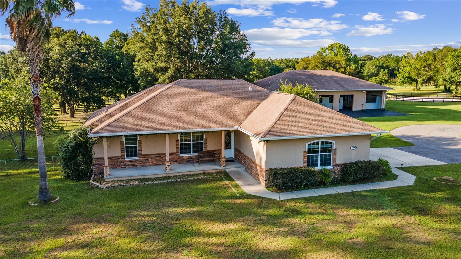 Discover the ultimate equestrian paradise on 20 meticulously maintained acres at 14401 and 14407 W Hwy 328. This sprawling estate boasts two distinct homes and exceptional equestrian amenities, making it a dream for horse enthusiasts and those seeking a serene country lifestyle. Located only 10 miles from the World Equestrian Center
The main home offers expansive living with 2,600 square feet of open-concept space. Highlights include engineered hardwood floors, modern appliances, and stunning granite countertops. The heart of the home is a remarkable 16’x46’ enclosed entertainment room, complete with a gas stainless steel grill, wet bar, and ample space for gatherings and relaxation.
The secondary residence, a beautifully updated 3-bedroom, 2-bath home, features a spacious split floor plan with elegant tile flooring throughout. Enjoy the modern touches of granite countertops, high ceilings, and an inviting 10x16 enclosed Florida room. Perfect for entertaining, the open layout seamlessly blends comfort and style.
Equine enthusiasts will appreciate the state-of-the-art 80x50 concrete barn featuring 9 stalls, including four 12x14 stalls and five 12x12 stalls. A separate air-conditioned tack room with a bathroom, a convenient feed room, and a wash area with water in the stalls ensure comfort and convenience for both horses and caretakers. A fly spray system adds to the thoughtful details of this equestrian haven.
Outdoor amenities abound with a 36x72 pole barn for equipment or additional stalls, a 30x45 metal equipment building, and a professionally built 150’x220 concrete-fines/clay sand mix arena. The property is fully fenced with 3-board fencing, offering several paddocks and turnout areas, alongside a round pen for training and exercise.
Nestled among majestic oak trees and gently rolling terrain, this property provides a picturesque backdrop for country living. With three wells on-site and an RV hookup, convenience meets tranquility in this exceptional equestrian estate.
Don’t miss your chance to own this extraordinary property offering luxury, comfort, and unparalleled amenities for both horses and homeowners alike. Schedule your private tour today and experience the comfort and rewards of Equestrian farm living at its finest.