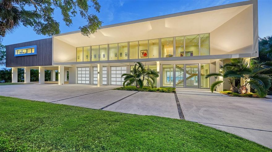 A modern masterpiece on Sarasota Bay, this architectural landmark embodies contemporary design and sustainable luxury. Set on over an acre in the prestigious Indian Beach neighborhood—Sarasota’s renowned “Museum Area”—the gated estate boasts nearly 180 feet of waterfront with panoramic views that extend endlessly across the Bay.
Conceived by acclaimed architect Mark Sultana of DSDG and expertly built by Voigt Brothers, the elevated residence rests gracefully on monumental columns, appearing to float above the landscape. Open-air colonnades below provide serene shaded spaces and complete storm protection, while the reinforced concrete structure—including the roof—ensures enduring strength. Elegant wood accents and striking architectural details bring warmth and balance to its modern aesthetic.
A powerful solar array crowns the home’s concrete roof, allowing fully off-grid operation. Beyond the oversized glass pivot door, a suspended staircase with solid wood treads and an elevator ascends to the main living level. Inside, walls of floor-to-ceiling impact glass frame mesmerizing water views from every room. The expansive great room transitions seamlessly to a vast covered terrace, creating a breathtaking indoor-outdoor living experience.
The sleek chef’s kitchen—enhanced by movable glass partitions—easily shifts from an open-concept entertainer’s dream to an intimate culinary retreat. The primary suite, privately positioned on the southern wing, offers inspiring views of the Ringling Bridge and includes a tranquil study. Along a sunlit gallery, four generous guest suites open to a full-length veranda overlooking Longboat Key and the Bay, with spa-like baths designed to let the water remain ever-present.
On the ground level, a four-car garage, ample storage, bonus space, and a shaded lounge connect to the dramatic 60-foot heated wet-edge lap pool—its horizon line merging with the sparkling city skyline. Just minutes from Downtown Sarasota, St. Armands Circle, Lido Beach, and celebrated cultural landmarks, this solar-powered sanctuary redefines coastal contemporary living, where architecture, innovation, and nature unite in perfect harmony.