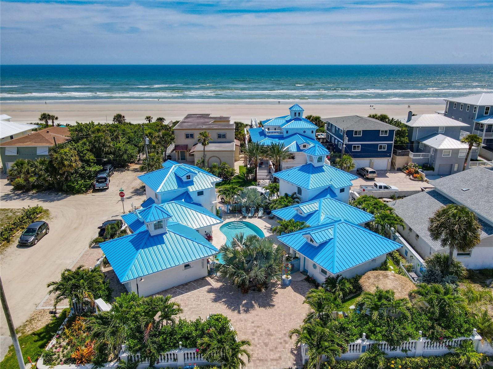 A rare chance to acquire Joy by the Sea - New Smyrna Beach’s premier 5-star luxury vacation resort. This exclusive direct oceanfront property combines a fully renovated (2021) coastal estate with six upscale beachside villas and a direct oceanfront 4 bedroom, 4 bathroom pool home, creating a truly one-of-a-kind boutique resort experience. Spanning two lots in the heart of New Smyrna’s highly sought-after short-term rental district, Joy by the Sea offers unmatched flexibility and proven income performance. The private oceanfront home delivers unobstructed views, private beach access, and a resort-style pool and spa with a volleyball net, surrounded by expansive decks designed for entertaining and relaxation. Inside, you’ll find elegant living spaces, two balconies with breathtaking ocean views, an elevator, a fully stocked kitchen with a Nespresso machine, and four beautifully appointed bedrooms: a king suite with stunning ocean views, a wine chiller/beverage fridge and a Nespresso machine, a twin bedroom with a small private balcony, a queen bedroom, and an additional twin room. Outdoors, enjoy a covered patio with a dining table, a hot tub, lounge seating, and an outdoor kitchen featuring two built-in green egg grills, a custom-built concrete pizza oven, a custom-built large charcoal or wood fire grill, a beverage fridge, and a nine-person bar top. The home is also equipped with 5 Smart TVs and offers driveway parking for your vehicles. Directly across the street, six fully furnished bungalow-style villas surround a private saltwater pool and tropical courtyard, offering additional high-end accommodations. The villas include two one-bedroom units, each sleeping up to eight guests, and four studio villas, each accommodating four guests. Every bungalow features a fully equipped kitchen with a microwave oven, stove, sink, full-size refrigerator, and stackable washer and dryers, making them perfect for extended stays. Both the Ocean Front home and the six studio villas are backed up by 3 Generac Guardian 26kW Aluminum Home Standby Generators to ensure a comfortable stay during Florida's unpredictable weather. Celebrated for its impeccable design, premium finishes, and exceptional guest reviews, Joy by the Sea is ideal for family reunions, luxury vacations, weddings, corporate gatherings, and special events. Offered fully turnkey, the property conveys with all furniture, décor, and appliances, making it truly move-in ready. The oceanfront home provides private beach access, while the bungalows are just steps away from public beach access. Whether you’re seeking a trophy asset, a high-yield rental property, a private coastal retreat, or a strategic 1031 exchange, Joy by the Sea’s boutique scale, iconic presence, and turnkey condition make it one of Florida’s most unique and recognizable oceanfront properties. Offered as a complete package, this is an extraordinary opportunity to own a true coastal gem.