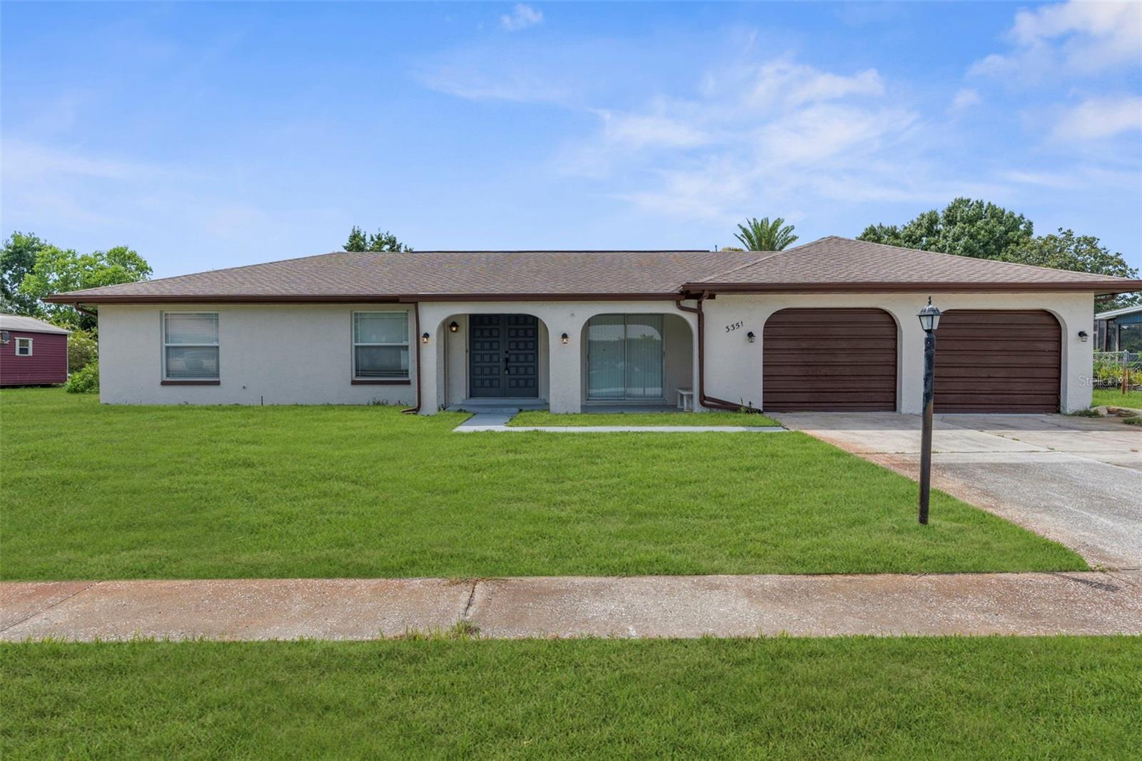 One or more photo(s) has been virtually staged. Natural beauty & neighborhood charm await- in this delighfully remodeled Hernando County getaway! Located in the heart of Spring Hill, 3351 Lambert Avenue is a 4-bed, 2-bath pool home that backs to Lake Teresa — a private grass-bed lake offering seasonal water views, stunning sunsets, and front-row seats to local wildlife. The 36-panel solid wood double door entry sets this home apart from the norm and offers a covered porch for plants or seating. Inside, a beautiful feature wall graces the entry, which opens to a spacious living room and dining area. One of our favorite places in this home is the stunning kitchen- completely updated with quartz counters and a large island, clean white cabinetry, newer stainless steel appliances, and a sleek modern sink. This thoughtfully designed split floor plan offers added privacy with the primary suite separated from the guest bedrooms. The primary bath has also been fully upgraded with luxe finishes, like the updated floor-to-ceiling marble walk-in shower! A versatile fourth bedroom features its own private entrance from the garage or lanai—ideal for multi-generational living, a home office, creative studio, or potential rental space. The 3-car garage allows even more room for storage; bring your golf cart, kayaks and more! Just minutes from Weeki Wachee Springs, Gulf beaches, and nature parks — this home blends quiet living with endless fun right around the corner. New roof (2017), and new A/C (2019)
