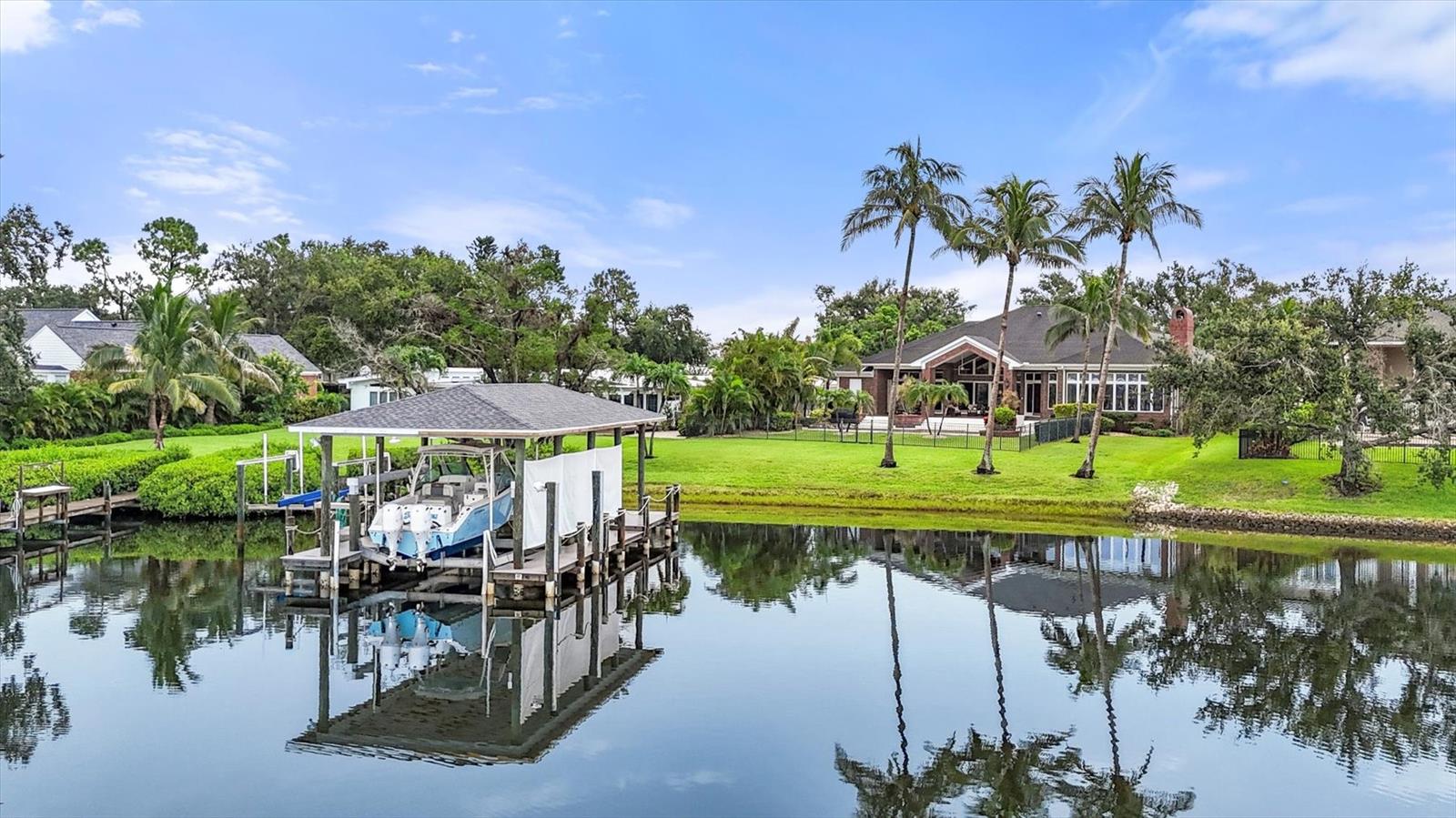 A boater’s tropical paradise awaits you in this custom-built home located on Warner’s West Bayou in desirable NW Bradenton. Imagine living the FL boating lifestyle where you can be out in your boat fishing or sightseeing in the beautiful Tampa Bay in a matter of minutes. This luxurious estate home features 4025 sq ft with 3 bedrooms + den with 2 full baths + 2 half baths plus an oversized saltwater pool on a boatable waterfront lot. This beautiful home sits on an estate sized lot with 100’ of water frontage and no HOA. There is a large covered dock that includes two boat lifts, one that is covered and fits a 50’ yacht, 25,000lb lift, with water & electric & a fish cleaning station. Coming into the home are beautiful mahogany double doors with glass inserts that welcome you and set the scene for elegant living. Upon entering the home, you will love the open floor plan with its high ceilings and beautiful water views. The living and dining rooms are inviting, spacious, and feature wood floors, elegant crown moldings, chair rails and custom built-ins. To enjoy large gatherings and family fun there is an impressive, oversized family room/game room with woodburning fireplace and large windows that let in the sunshine, pool, and water views. The spacious kitchen which opens to the family room is a chef’s dream with wood cabinetry, granite countertops, tile backsplash, newer stainless-steel appliances, a large center island with prep sink, and a built-in desk. Rest and relax in the master bedroom suite overlooking the lovely backyard with sliding doors opening to the pool area and water views. The master bath features travertine floors, a large walk-in shower and large tub made for two. Separated from the master bedroom are two spacious bedrooms and a hall bathroom with tub and walk in shower. Next is the laundry room that is oversized featuring a newer washer & dryer, laundry sink, plenty of cabinets and a large closet. Out back everyone will love the oversized covered lanai that is a dream come true and keeps you shaded during the day while your family is enjoying the sunshine in the pool and spa. There is a pool bath and an outside shower plus a storage closet for all your boating gear. Watching the sunsets views while sitting on the lanai with your favorite beverage is a lovely way to end the evening. The backyard is fenced for your family and pets to run and play and there is an open beach for kayaking or canoeing. Another great feature is the oversized 40’ 3 car insulated A/C’d garage with large semi-circular driveway with parking area. Plenty of room to park, store your possessions, and work on your cars. All this is conveniently located to Sarasota/Bradenton airport, IMG Academy, restaurants, shopping, and the beautiful AMI Gulf beaches.