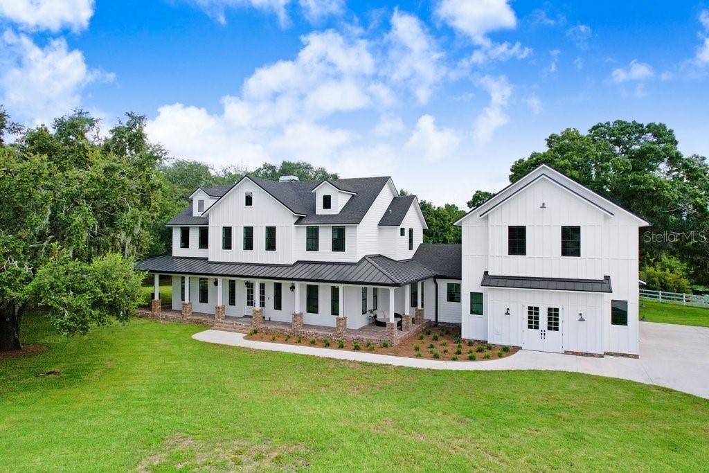 Welcome to an extraordinary 2023 built modern farmhouse estate, nestled at the end of a private cul-de-sac in the serene and picturesque Odessa, Florida. As you enter through the pristine white gate, the grandeur of this expansive home unfolds before you, set atop 6.62 acres of impeccably manicured land, offering stunning conservation and pond views. Step onto the beautiful, brick-paved wraparound porch and through the elegant white French doors, where you are greeted by an abundance of natural light and exquisitely crafted farmhouse details throughout. Just off the foyer, double barn doors open to a sophisticated formal dining room, perfect for hosting elegant gatherings. The open-concept design seamlessly flows into a massive kitchen, anchored by an oversized center island complete with a double dishwasher and a spacious single-well sink. Culinary enthusiasts will appreciate the artful blend of functionality and style with a Big Chill Classic matte black refrigerator, a Hallman six-range gas burner stove with griddle, and a charming farmhouse apron sink with a drying rack that overlooks the lush backyard. Nearby, a meticulously organized walk-in pantry adds to the home's thoughtful design. The living room is a true centerpiece, featuring soaring cathedral ceilings, exposed wooden beams, a cozy fireplace, and three sets of double doors that invite you to step out into your backyard oasis which is a true sanctuary, featuring a covered seating and grilling area with large ceiling fans, a sparkling saltwater pool and spa, all surrounded by lush greenery and private conservation. The spacious primary suite offers direct access to the backyard, his-and-hers walk-in closets, and a luxurious en-suite bathroom with dual vanities, an oversized walk-in shower with a waterfall feature, and a farmhouse-style soaking tub. Convenience is key, with a first-floor oversized laundry room that makes laundry day a breeze. Upstairs, a cozy loft area provides a welcoming retreat for guests, along with three spacious guest bedrooms, two of which share a charming Jack-and-Jill bathroom. Then, on the opposite side of the home, an additional upstairs bonus suite with a full bathroom offers versatility as an extra guest retreat, gym, or more. This home effortlessly blends elegance and practicality with features like porcelain wood plank tile floors, impact windows, Navien tankless water heaters, three HVAC units, and a spacious three-car garage. It is a rare find that offers both refined sophistication and modern comfort in a tranquil, idyllic setting. Recent upgrades by current owners include fencing, gutters, irrigation system, electric blinds, mosquito misting system, major landscaping and water filtration system. Odessa is located just north of Tampa, making it conveniently close to the city's amenities, including Tampa International airport, International Plaza, Michelin Star restaurants and other fine dining, cultural attractions such as Busch Gardens and the Tampa Zoo, amazing beaches & waterways, and professional sports such as The Tampa Bay Buccaneers, Tampa Bay Lightning, The rays and Tampa Bay Rowdies. The proximity to Tampa allows residents to enjoy the best of both worlds—tranquil living with easy access to urban conveniences. Copy Floorplan and survey (prior to fencing) available for review.
