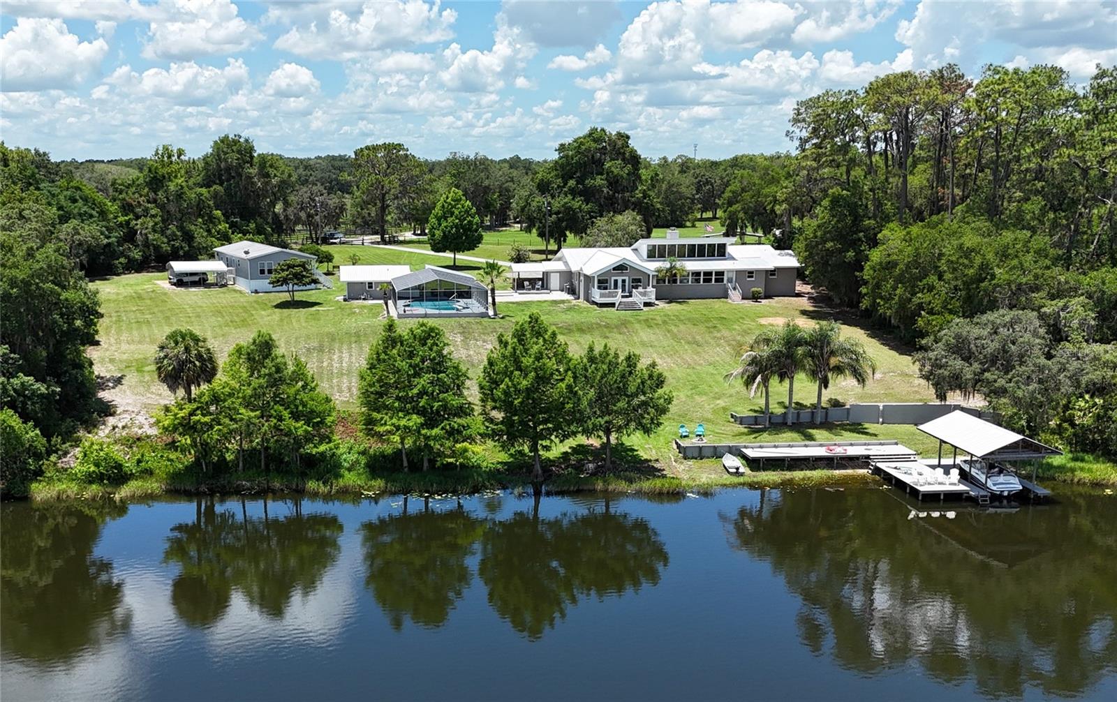 Premier Lakefront Living — Where Elegance Meets Tranquility
Experience the perfect blend of elegance and rural charm with this stunning lakefront estate featuring over 500 feet of private, spring-fed shoreline on Lake Fay. Situated on 14.75± acres and zoned A1, the property is ideal for equestrian or cattle use. The fully remodeled main residence includes a custom addition designed to capture natural light and panoramic views from sunrise to sunset. The spacious living area features a stone wood-burning fireplace, and the open-concept kitchen flows seamlessly into a large dining area, perfect for entertaining. The luxurious owner’s suite offers a gas fireplace, vaulted ceilings, French doors, expansive windows with private deck access, a coffee and wine bar, an elegant marble bathroom with dual vanities and a spa-style shower, and a 14' x 14' walk-in closet. The home also includes a second ensuite, plus two additional generously sized bedrooms, each with walk-in closets and thoughtful separation for privacy. Outdoor amenities include a screened 9-foot-deep pool, a cabana, an outdoor kitchen, and incredible pool-to-lake infinity views. A private dock with sun deck and boat lift enhances lakeside living. Additional features include a newer metal roof, three A/C zones, water softeners, Icynene insulation, a separate 2BR/2BA guest house with its own well and septic, a 60' x 40' equipment barn, an open-air two-stall barn, and fully fenced and gated grounds. This exceptional property is a rare opportunity for those seeking luxury, privacy, and space, just 20 minutes from The Villages.