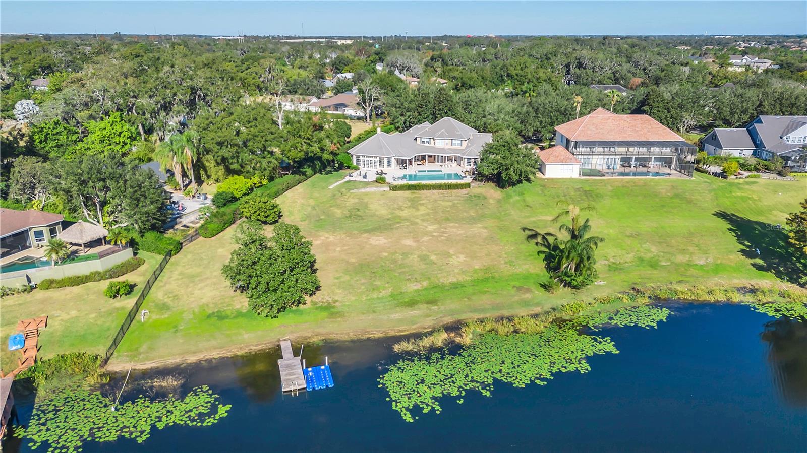 Private Lakeside Paradise! Nestled within a coveted gated enclave of only 13 estate homes, this breathtaking residence by Kelsey Custom Homes offers unparalleled luxury with sweeping views of Lake Olivia. Situated on a prime corner lot, this exquisite 5-bedroom, 6.5-bathroom (plus upstairs media room) estate encompasses over 6,200 square feet of opulent living space including a three-car garage and stunning pool. The main level features a living room, dining room, primary suite and guest bedroom, kitchen overlooking the family room and oversized sunroom. Enter to a dramatic foyer with a sweeping staircase and gleaming hardwood floors creating an atmosphere of sophistication. Designed for the discerning chef, the kitchen features Taj Mahal quartzite countertops, cherrywood cabinets, a pot filler, wine refrigerator, farmhouse sink with insta-hot feature, and luxury Bosch and Wolf appliances in 2021, including double ovens, convection microwave and a walk-in pantry. The kitchen overlooks the spacious family room, which features a cozy fireplace that can be used as either a gas or wood-burning unit. The family room flows effortlessly into the bright and airy Florida room, with panoramic lake views as the backdrop. The main-level guest suite offers comfort and convenience with retractable shades, an en-suite bath and direct access to the expansive Florida room. The split floor plan ensures privacy, with the primary suite tucked away to include a spacious sitting area, inlaid crown molding with accent lighting and a massive walk-in closet that's more like a room of its own, complete with a separate storage area. The luxurious bath is a retreat, featuring a jetted Jacuzzi soaking tub, a separate rain shower, in-mirror TV and dual vanities for added elegance and functionality. A second staircase leads to the upper level, featuring three additional bedrooms, two with en-suite baths, and three full baths, plus a sizable bonus/theater room, ideal for movie nights. The outdoor spaces of this home are nothing short of extraordinary, offering an expansive 3,000-square-foot patio including a fire pit that is an entertainer’s paradise. The outdoor kitchen is equipped with a barbecue grill, flat top cooktop, mini refrigerator, sink and is plumbed for gas, making it ideal for hosting outdoor functions. For added entertainment, the space includes an outdoor TV and a built-in sound system, setting the ambiance for relaxed evenings or lively gatherings. The sparkling saltwater pool, installed in 2021, features an impressively sized 20-foot Jacuzzi, tranquil water bowl fountains and offers breathtaking views of the peaceful waterfront. The backyard also includes built-in mosquito misters, allowing you to enjoy the outdoors in complete comfort with no screens needed. Whether you're lounging by the pool, dining alfresco or simply taking in the local wildlife, this private oasis has been designed to elevate every experience. Store your toys in the three-garage equipped with a Level Two electric vehicle charger, oversized storage space and custom built-ins. Additional features include a full-house soft water system my Kinetico. Conveniently 25 minutes from Disney, 20 minutes from Universal, less than 15 minutes from the historic/shopping area of Windermere, 20 minutes to downtown Orlando and 30 minutes to MCO. This magnificent property effortlessly combines opulence with the comfort of everyday living; schedule your showing today!