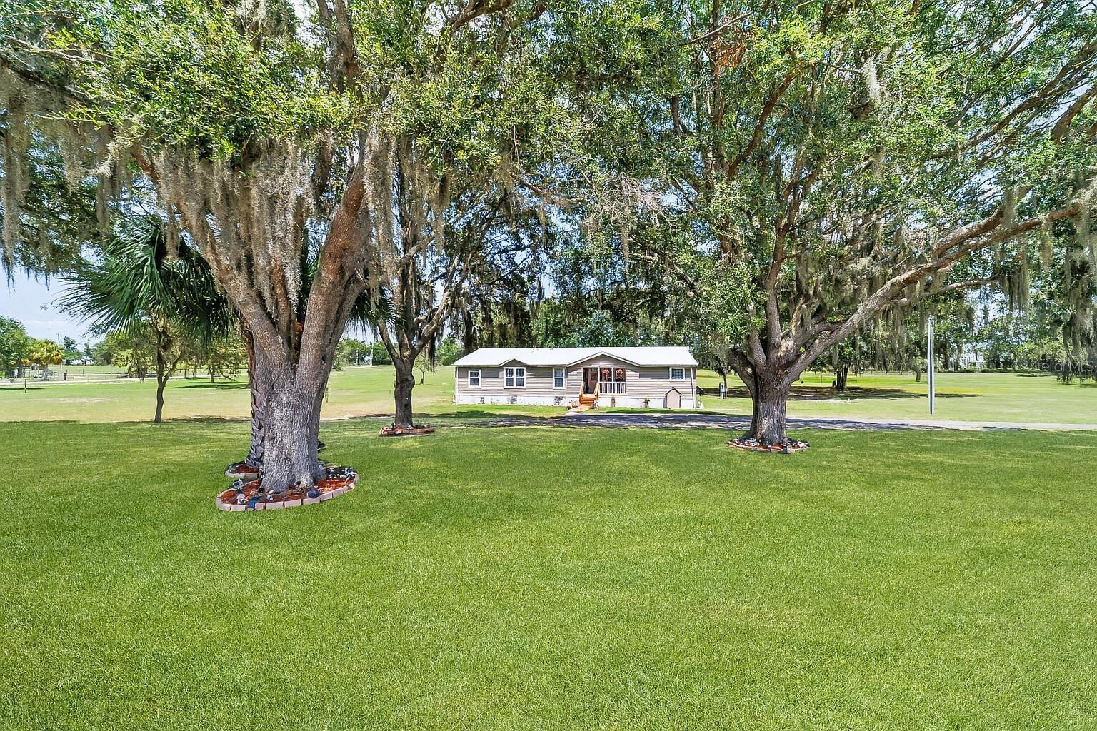 Luxury Custom Triple-Wide on 10 Acres – Dunnellon, FL
Luxury custom triple-wide on 10 beautiful acres, this 4-bedroom, 3-bathroom home offers over 2,500 sq ft of thoughtfully designed living space and a lifestyle that blends high-end comfort with peaceful country charm. Built in 2022, the home features a spacious open floor plan, ideal for entertaining and everyday living. The large kitchen is the heart of the home, complete with smart appliances, white cabinetry, neutral tones, ample counter space, and an oversized bar with a farmhouse sink that adds to the warm, inviting feel. Large windows flood the space with natural light, offering beautiful views in every direction.
The split floor plan creates ideal separation between living areas. The master suite is a true retreat, complete with a bonus sitting room, large walk-in closet, spa-style bathroom with a sunken tub and double vanities, and private sliding glass doors that lead to the outdoors. On the opposite end of the home, you'll find a guest bedroom and bathroom, and across the kitchen, another wing features a formal dining room, an additional guest bedroom with full bath, and a second master suite—perfect for multi-generational living or hosting guests.
Step outside and enjoy the expansive back deck with views of the lush green pastures and tranquil landscape. A wooden walkway leads to the vibrant pool area, where an above-ground pool is surrounded by an oversized party deck—ideal for entertaining, relaxing, or sunbathing in total privacy. Just beside the pool is a cheerful outdoor changing cabana with its own bathroom and shower—brightly colored and perfectly reminiscent of island vibes.
Beyond the pool, you’ll find a screened garden for growing vegetables, a stone-and-mulched pathway to the cozy firepit with stump seating under the shade of scattered oaks, and an outdoor kitchen overlooking a peaceful pond—perfect for grilling and winding down the day. The property features roughly 50 mature oaks that provide natural beauty and shade, as well as a second storage building, RV pad with 50-amp power, and additional outbuildings for storing equipment and tools. The main storage building includes wings on each side for tractors, implements, or trailers.
The home sits back from the road with a paved driveway and parking area, and the front porch with pavers offers the perfect spot to enjoy Florida’s stunning sunsets. Located on a paved county road in a quiet rural setting, this property offers both privacy and convenience.
Enjoy nearby outdoor adventures with Goethe State Forest just minutes away, offering miles of horseback riding and walking trails, and the crystal-clear, 72-degree waters of Rainbow Springs and the Rainbow River perfect for kayaking, tubing, and swimming. You’re also just a short drive to shopping, dining, and daily conveniences in Dunnellon and Williston, and within easy reach of Ocala, Gainesville, and the Gulf Coast.
Whether you're seeking a private retreat, a family homestead, or a place to entertain and enjoy nature, this is the perfect blend of luxury, functionality, and laid-back Florida living.
