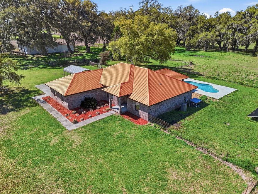 Escape to the peaceful charm of country living with this beautifully updated 3-bedroom, 2-bathroom brick home with a pool, perfectly situated on over 10 picturesque acres along a paved road. Surrounded by mature oak trees and serene views, this property offers privacy, space, and modern upgrades all in one. Step inside to find new flooring, renovated bathrooms, and brand-new appliances, along with a NEW HVAC system and NEW copper metal roof, giving you peace of mind for years to come. The spacious living room features sliding glass doors that open to a covered back porch overlooking the solar heated salt water pool—the perfect place to relax, entertain, and take in the beautiful countryside views. The home offers a thoughtful split floor plan, with the private primary suite on one side and the additional bedrooms on the other. The primary bathroom features a large soaking tub, ideal for unwinding after a long day. The spacious kitchen provides ample cabinet storage, along with a formal dining area, eat-in kitchen space, and bar seating, making it perfect for gatherings and everyday living. Outside, the property truly shines with a massive enclosed barn with bays, plus an attached garage and carport, offering plenty of room for equipment, hobbies, animals, or all of your recreational toys. The fenced acreage provides endless opportunities for farming, homesteading, or simply enjoying wide-open space. If you’re looking for peaceful, private country living with modern upgrades and room to roam, this exceptional property is a must-see.