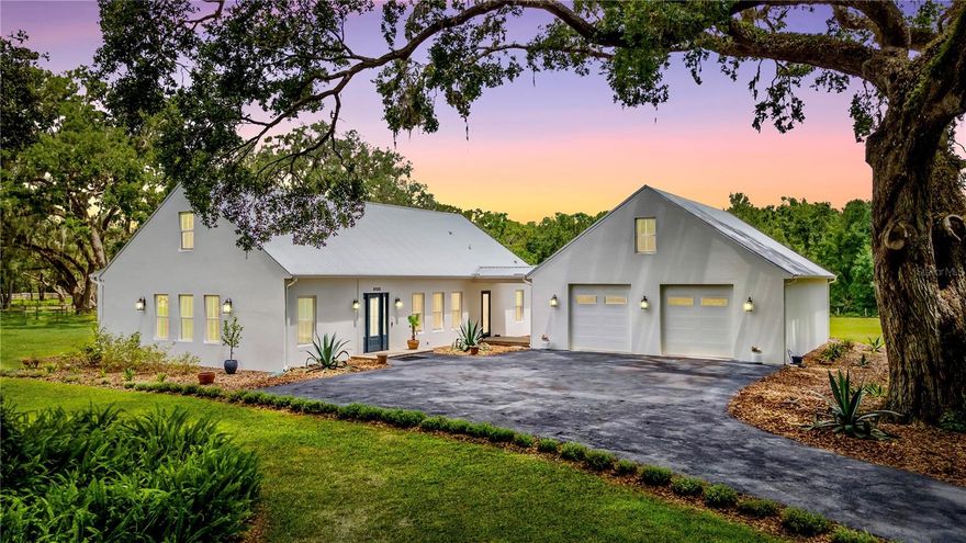This exceptional custom estate at 31035 Pasco Rd. offers the perfect blend of quiet luxury, modern efficiency, and room to grow. Set on 3.35 private acres at the end of a picturesque 500-foot driveway lined with young white myrtles beneath majestic grandfather oaks, this property delivers both serenity and an impressive sense of arrival.

Thoughtfully designed and quality-built, the home features 4 bedrooms, 5 bathrooms, 6 car-garage and 2,976 square feet of beautifully maintained living space, including a flexible split floor plan with a private mother-in-law suite. The expansive great room flows seamlessly into the outdoor living area through towering sliding glass doors that fully open to a stunning covered porch—complete with a gas fireplace and TV—perfect for entertaining or enjoying breathtaking sunset views year-round.

At the heart of the home, the chef’s kitchen is anchored by an oversized quartz island and equipped with a 5-burner gas cooktop, built-in oven, and pot filler—ideal for both everyday living and hosting. The luxurious primary suite offers direct porch access and features dual vanities, generous his-and-her closets, a deep soaking tub with air jets, a walk-in shower, and a private water closet. Two additional bedrooms share a Jack-and-Jill bath, while a third full bath provides convenient access to the outdoor living space. Both the primary and third bathrooms are thoughtfully designed for wheelchair accessibility.

Car enthusiasts and hobbyists will appreciate the oversized 6-car garage with ample ceiling height for a car lift. Additional highlights include a large laundry room with sink and storage, climate-controlled attic space for excellent opportunity for a 5th bedroom, office, or bonus room and a tankless gas water heater ensuring endless hot water.

Ideally located just minutes from Interstate 75, everyday conveniences like Publix, local dining, and nearby parks are easily accessible—offering the perfect balance of peaceful country living and modern-day convenience.

This is a rare opportunity to own a one-of-a-kind estate that truly has it all—space, luxury, privacy, and functionality. Schedule your private showing today and experience it for yourself.