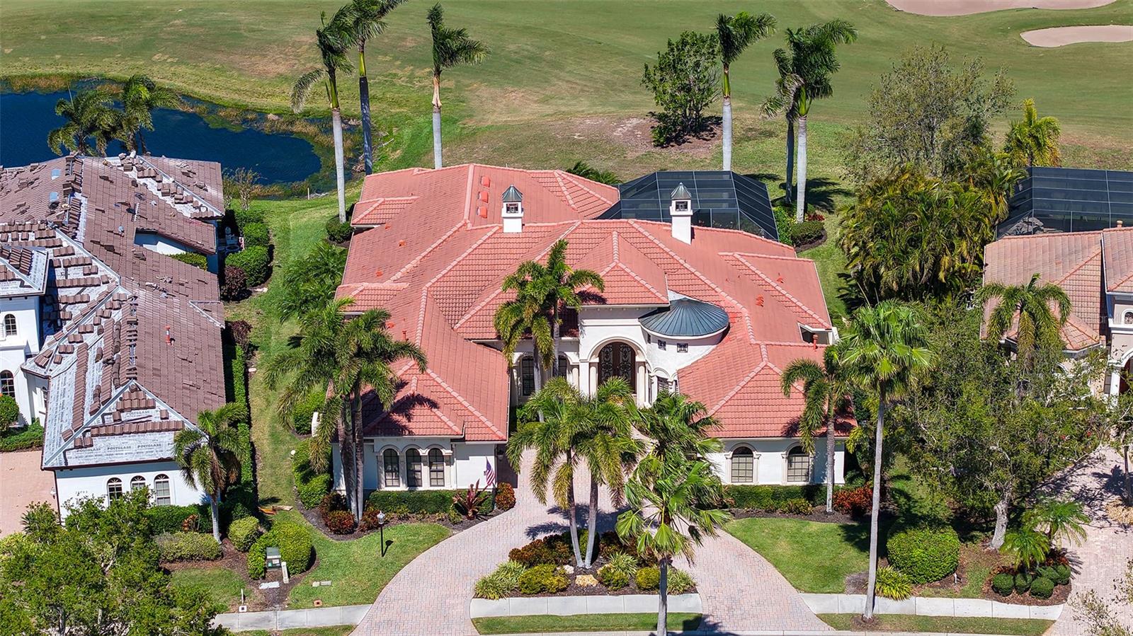 Unparalleled elegance and design on a stunning golf course setting! Perfectly positioned on one of Lakewood Ranch Country Club's premier homesites this tastefully updated Lee Wetherington home offers unobstructed lake and golf course views of the 14th fairway on the King's Dunes Course. Upon entering the massive iron and glass double doors you will notice the soaring coffered ceilings, beautiful aquarium windows framing picturesque views of the pool and golf course, warm walnut hardwood flooring throughout the main living areas, and elegant cast stone fireplace adorning the living room. The great room boasts high ceiling with wood timber beams and provides abundant space and natural light for hosting family and friends. Massive, disappearing sliding-glass, impact rated doors bring the outdoors in, providing open access to the amazing pool and outdoor entertaining spaces! Sharing this space is the large gourmet kitchen showcasing refinished cabinetry with under and over-cabinet lighting, a floating island, warm granite countertops, a discrete walk-in pantry, a GE Monogram gas 6 burner cooktop, a beverage cooler and a new oversized GE Monogram refrigerator. Beyond the great room you will find huge solid wood doors that lead to the state of the art, sound engineered movie theatre with remote blackout shades, wood paneling from floor to ceiling, plus an artful ceiling detail with custom lighting. The 3 incredibly sized additional guest bedrooms provide a quiet domain for family visits while ensuring privacy from the main house. The owner's suite boasts amazing views to the lanai, pool and golf course while disappearing sliding doors bring in an abundance light and beautiful Florida breezes. The primary suit also offers 2 spacious walk-in closets with custom built-ins, a spa-like bath, including dual vanities, a soaking tub and a walk-in shower, all recently renovated. A soothing garden shower brings in natural light and offers beauty and privacy for those thrilling outdoor showers.
The enormous lanai displays design perfection complete with abundant space to relish the perfect outdoor setting. Travertine pavers adorn the entire lanai, and the glass enclosed outdoor entertaining space offers a fully equipped outdoor kitchen, with an ice maker, stainless steel Lynx gas grill, beverage refrigerator and sink. The refreshing saltwater pool and a spa are framed by the panoramic screening to enjoy the obstructed gorgeous golf course, lake and preserve views. This amazing home also features double 2-car garages with additional storage, 2 gas hot water heaters, and the added bonus of air-conditioning for one of the garages. ** This home is being sold with furnishings presented, as a convenience to the Seller at no added value, except the recliner in the movie theater. **
Lakewood Ranch Country Club offers the ultimate Florida lifestyle with a private country club with 3 luxurious clubhouses, 4 golf courses, 18 Hard-Tru lighted tennis courts, pickleball courts, state of the art fitness center, aquatic center, parks, walking trails and so much more. Membership is optional and no waitlist. All within minutes of the UTC Mall, fabulous dining and shops, Lakewood Ranch Main Street, polo fields, Benderson Park, and the much-anticipated new home for Mote Marine Aquarium. Plus, don't forget you're only a short drive to the world's top-rated beaches! This is truly luxury at its finest, schedule your private showing today.