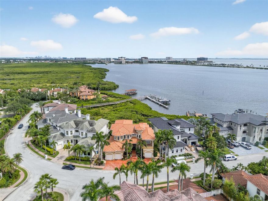 Welcome to The Reserve of Old Tampa Bay—Tampa Bay’s most coveted gated waterfront enclave, where timeless elegance meets resort-style living. Tucked away behind lush tropical palms, this renowned community offers unparalleled privacy, direct water access, and the kind of sunrises and sunsets that define Florida’s West Coast lifestyle. Custom-built in 2006 by the esteemed Alvarez Homes, this architectural masterpiece makes an unforgettable impression from the moment you arrive, as double custom entry doors open into a grand two-story foyer crowned by a dazzling crystal chandelier. To the left, an elegant formal dining room sets the stage for exquisite dinner parties, while the formal living room offers dramatic floor-to-ceiling bay views anchored by a Baby Grand player piano. The first level is designed for both luxury and convenience, featuring a guest or mini-owner’s suite complete with a private balcony perfect for morning coffee with serene views, direct poolside access, an ensuite bath, and a walk-in closet—ideal for multigenerational living or extended stays. A statement powder room showcases an artistic floor-to-ceiling Florida mural, while a discreet private entrance to the one-car garage ensures privacy. The chef’s kitchen is nothing short of extraordinary, outfitted with professional-grade appliances including a Wolf gas cooktop, Bosch convection oven, Profile microwave, Sub-Zero refrigerator, wine chiller, and Bosch dishwasher, all complemented by custom cabinetry, granite counters, and an expansive island that elevate both form and function. Nearby, the laundry suite connects to a two-car garage with a custom lift, tankless water heater, water softener, and reverse osmosis system. Designed for entertaining, the open-concept family and dining areas boast custom built-ins, an in-house audio system, and fully pocketing glass sliders that dissolve the boundary between indoor luxury and outdoor splendor. Step onto the expansive patio and experience resort living at its finest with a private heated saltwater pool, cascading spa, and sauna, all framed by panoramic bay views, while a poolside half bath and fully equipped outdoor kitchen—complete with granite bar, counter seating, and gas grill—make alfresco entertaining effortless. After dinner, launch your boat from the private lift and cruise the sparkling waters of Old Tampa Bay. Ascending via the chandelier-lit elevator, the second level is equally impressive, with a dramatic catwalk leading to two spacious guest suites, each with walk-in closets, a shared Jack-and-Jill bath, and private balconies. Across the way, a loft and bonus room conceal a hidden passage to the show-stopping primary suite, where indulgence awaits in a spa-inspired retreat featuring dual vanities, two private water closets, a deep jetted soaking tub, and a grand walk-in shower. Additional upgrades include a brand-new metal roof, ensuring long-lasting durability and peace of mind. Just minutes from Downtown Tampa, the Gulf Beaches, and Tampa International Airport, The Reserve of Old Tampa Bay offers the perfect balance of exclusivity and convenience—more than a residence, it is a statement of prestige, comfort, and unparalleled waterfront living.