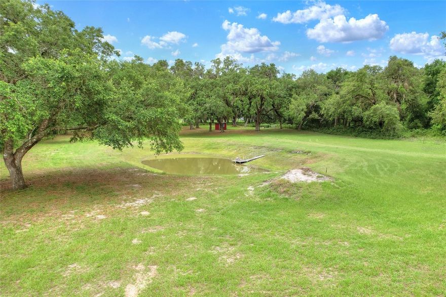 Tucked beneath a cathedral of Grandfather Oaks draped in Spanish moss in the heart of Bushnell, Wagon Wheel Ranch is more than land. It is a living canvas for your legacy. This 13.41-acre RR5C property blends the soul of Old Florida with wide-open potential, inviting you to dream bigger, live deeper, and build your next chapter on your own terms. A winding oak-canopied drive welcomes you into a uniquely C-shaped layout designed by nature and ideal for creating distinct zones for living, working, recreation, and privacy. With multiple cleared, buildable areas throughout, the land offers rare flexibility for a custom homestead, family compound, mini ranch, or agricultural use, with room to design multiple structures, access points, or future expansion. At the heart of the property sits a peaceful custom pond featuring a dock and seating area. It is the perfect place for sunrise coffee, quiet reflection, or sunset stillness. Fully fenced and livestock-ready, the property is equipped with both power and water already on site, allowing you to begin your vision with less delay and more momentum. Additional utility structures and concrete-floored carports provide functional support for equipment, storage, or day-to-day ranch operations. No HOA. No deed restrictions. Just freedom, and the rare opportunity to own a truly special piece of Florida land. Conveniently located near US-301, I-75, and SR-50, you are close to dining, shopping, and the natural beauty of the Withlacoochee State Forest, yet when you are here, the world feels miles away. 13.41 Acres | Fully Fenced | Zoned RR5C | Flood Zone X | Power and Water On Site | Multiple Build Sites | Pond with Dock and Seating Area | Carports with Utilities | No HOA and No Deed Restrictions Note: Any future commercial or event use (weddings, retreats, agritourism, or public venue operations) would require appropriate county permitting and zoning approval.