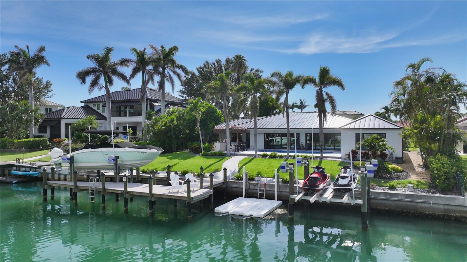 This striking waterfront Bird Key residence delivers a seamless blend of refined updates, thoughtful design, and effortless coastal living. Nestled along a wide canal just moments from Sarasota Bay, this four-bedroom home—with additional office—offers nearly 3,400 square feet of open living space, designed to showcase its serene water views and inviting indoor-outdoor lifestyle. Noteworthy enhancements include new roof in 2023, hurricane-impact windows and sliders, custom lighting, updated bathrooms, and a paver driveway framed by lush tropical landscaping. Step inside to a light-filled layout where wide-plank tile flooring flows throughout. At the heart of the home, the redesigned kitchen sets a stylish tone with crisp white cabinetry, quartz countertops, a massive island with bar seating, and premium stainless-steel appliances. A secondary counter area doubles as a coffee/wine bar or serving station—perfect for entertaining. The adjacent living and dining room is anchored by a custom paneled accent wall with fireplace and floating shelves, while oversized pocketing glass doors create a continuous connection to the expansive pool terrace and the water beyond. The split-bedroom plan enhances privacy, with the waterfront primary suite tucked away for maximum tranquility. Beautiful water views are complemented by a spa-like bathroom featuring dual vanities, glass-enclosed shower, and generous custom closets. Across the home, three additional guest bedrooms offer versatility. One is currently used as an office with a built-in Murphy bed; another includes its own en-suite bath and patio access—ideal for guests or multigenerational living. Outdoor entertaining takes center stage on the reimagined lanai, where a resurfaced heated swimming pool and expansive newer deck invite relaxation. Dine while relishing bay breezes, enjoy drinks at the custom tiki bar with built-in grill, or unwind at the water’s edge. A newer seawall (2005, repaired in 2025), newer dock (2023), dual 7,000-pound jet ski lifts, and 10,000-pound boat lift complete this boater’s paradise. Located on one of Sarasota’s most sought-after barrier islands, Bird Key offers private club amenities (with additional membership to the Bird Key Yacht Club), 24-hour security, and an unmatched central location. Just minutes from downtown Sarasota’s cultural attractions, St. Armands Circle’s boutique shopping and dining, and the white sands of Lido and Longboat Key beaches, this home is an extraordinary opportunity to live the Gulf Coast lifestyle with every comfort in place.