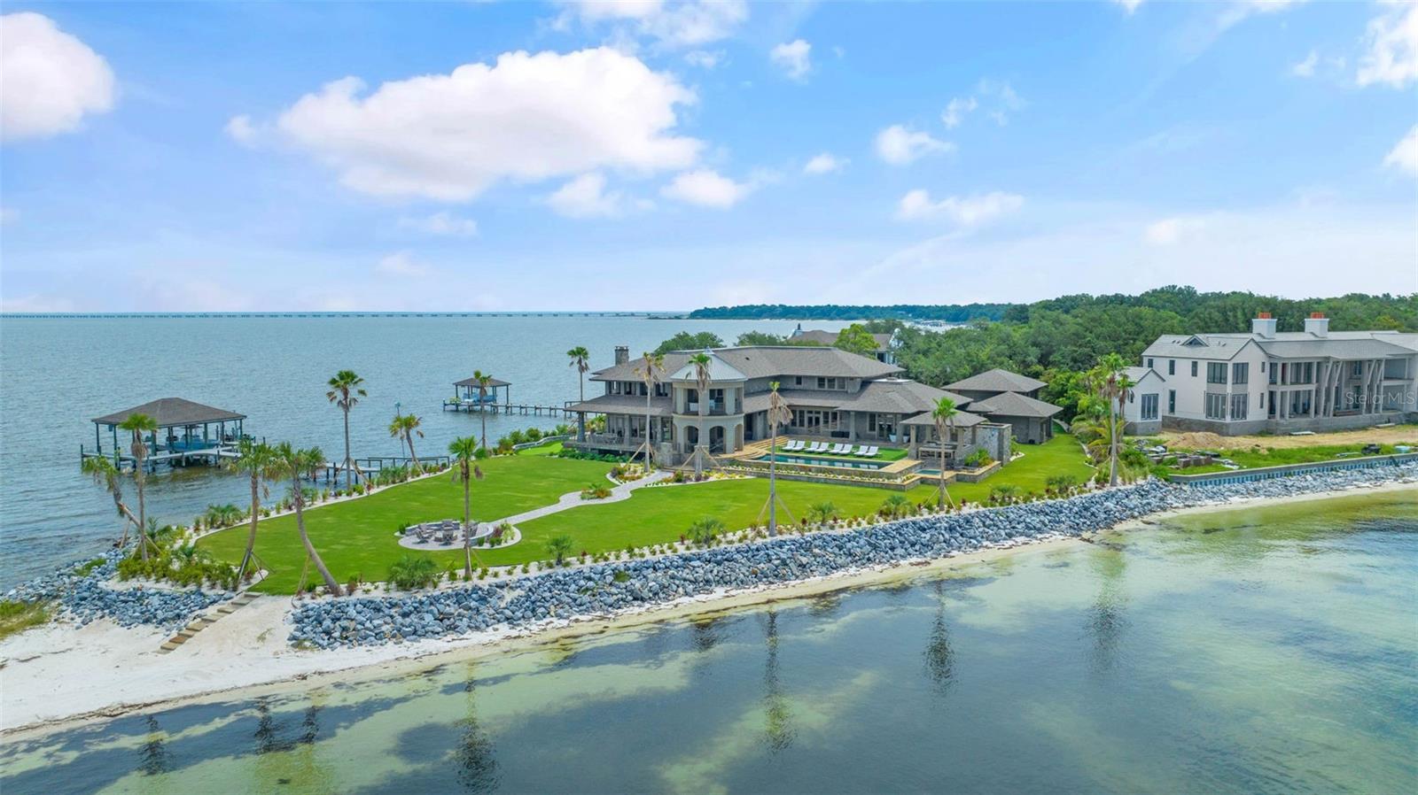Introducing an unparalleled waterfront sanctuary in Gulf Breeze, Florida! Situated on a coveted western-facing tip lot, this luxurious estate offers ultimate privacy and opulence. With over 12,000 square feet of living space and 1000 feet of water frontage, this home epitomizes waterfront luxury.
On the lower level, you’ll find a luxurious home theater designed for ultimate cinematic enjoyment. Nearby, a beautifully appointed bedroom suite and a spa-like bathroom offer a serene retreat. The sophisticated office provides a perfect workspace, while the well-equipped gym supports your fitness goals.
The expansive great room, flooded with natural light, showcases stunning views of the water and the meticulously maintained putting green, creating a perfect setting for relaxation and entertaining. Marvel at the panoramic 300° views of Pensacola Bay from every angle of the residence.
With breathtaking water views, the primary suite features a massive walk-in closet and a spa-like ensuite with both indoor and outdoor showers for ultimate privacy. A built-in espresso machine adds luxury and convenience, creating a serene retreat that blends comfort, elegance, and tranquility.
Outdoor enthusiasts will delight in the array of amenities, including a putting green, underground trampoline, boat and jet ski lift, private beach, and upgraded landscaping. Say goodbye to pesky bugs with the underground mosquito mister while you enjoy the saltwater pool and spa overlooking the serene waters. Entertain with ease in the outdoor kitchen, perfectly positioned to take advantage of the breathtaking views.
A detached apartment provides additional living space, complete with a full kitchen, bath, bedroom, washer, dryer and balcony, ideal for guests or extended family. This one-of-a-kind home offers a rare opportunity to experience waterfront living at its finest. Embrace the Gulf Breeze lifestyle in this exquisite retreat, where luxury meets tranquility.