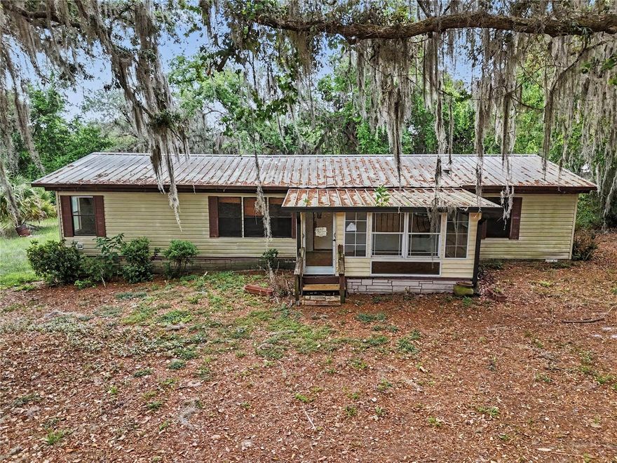 Tucked beneath a canopy of moss-draped oaks in rural Ocklawaha, this 3-bedroom, 2-bathroom manufactured home offers space, privacy, and room to breathe. The split floor plan features vaulted ceilings, an open living and dining area, and laminate wood flooring throughout the main living spaces. The eat-in kitchen includes oak cabinetry, a full appliance package, and a breakfast bar pass-through that opens to the dining area, perfect for casual entertaining. A large enclosed Florida room runs the length of the home with wall-to-wall windows and ceiling fans, ideal as a sunroom, office, or second living space, and a separate front bonus room adds even more flexibility for guests, hobbies, or a home gym. Outside, you'll find a detached covered carport with concrete pad (perfect for RVs, boats, or extra vehicles) plus a workshop/storage building, a partially fenced lot with cattle gate entry, mature oak canopy providing natural shade and privacy, a metal roof, and a dedicated interior laundry room. All of this in a quiet country setting just minutes from Lake Weir, the Ocklawaha River, and the Ocala National Forest, with easy access to Belleview, The Villages, and Ocala.