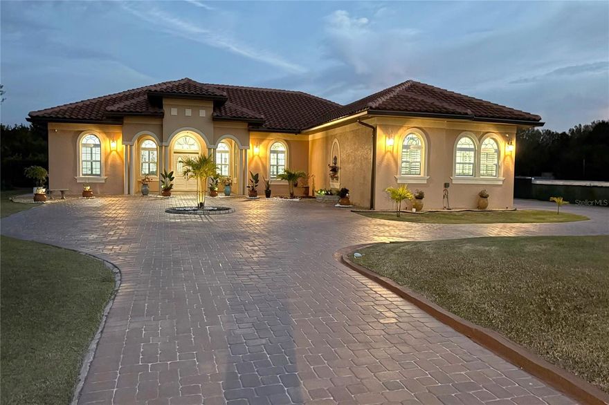 This custom-built residence seamlessly blends refined craftsmanship with resort-inspired amenities. Topped with a Spanish Mediterranean tile roof, it is on a fully fenced 0.9-acre homesite with a private electric gate and no homeowner's association. Designed with precision, the home features porcelain tile flooring throughout, impact-rated doors and windows, and plantation shutters, including in the garage. Encompassed by 125 feet of brick pavers, the grounds are as meticulously planned as the interiors. The outdoor living space centers around a saltwater pool framed by a hand-laid stone wall and anchored by a fully equipped, lighted tiki bar. This alfresco retreat includes a television, Bluetooth speakers, dual refrigerators, a grill, a fire pit and a heat pump heater for year-round enjoyment. Inside, the three-bedroom, three-bath residence includes 10-foot ceilings, motorized blinds, and a primary suite with an expansive walk-in closet. The gourmet kitchen is fitted with Smart LG appliances, Wi-Fi connectivity and a 14-by-5-foot island. Additional features include a beverage station with wine refrigeration, two pantries, a covered lanai and an oversized laundry room with built-in cabinetry. Technology and security are thoughtfully integrated with eight cameras and power access on each exterior corner. Architectural details such as tray ceilings, crown molding, arches and niches underscore the home’s elevated design. Near Disney, Medical City and Universal, this Central Florida residence offers exceptional access with uncompromising luxury. Seller is willing to consider closing cost contribution or interest buydown with a full offer.