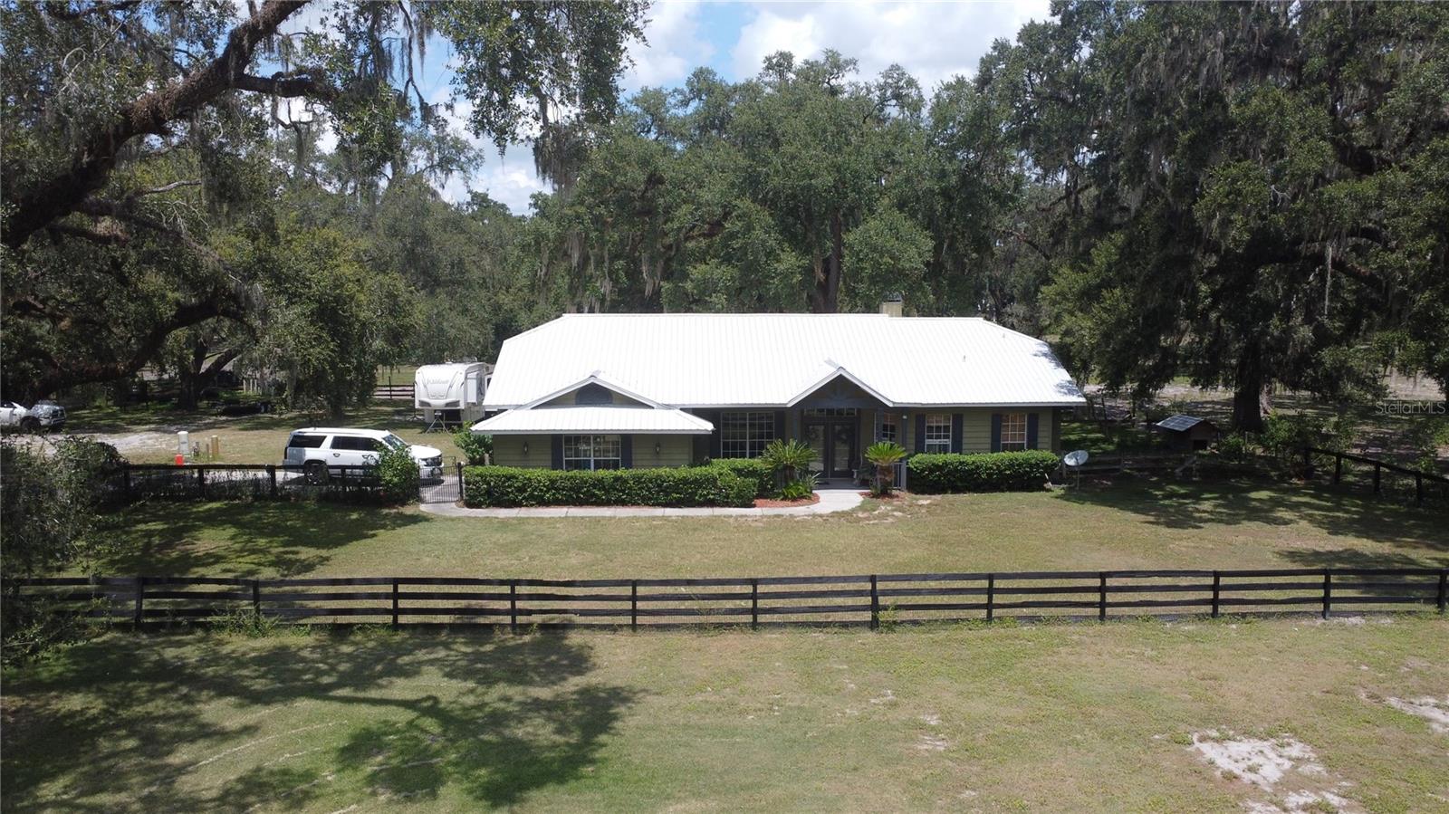 Escape to the country and enjoy the perfect blend of comfort and rural living on this beautiful 10-acre property. Located at the dead end of a paved road, you will be surrounded by majestic live oaks and the peaceful tranquility of quiet country living while still being convenient to town. The inviting 3-bedroom, 2-bathroom concrete block home offers an open concept living and dining room area with 14 ft ceilings and a cozy wood burning fireplace. Bright kitchen with ample storage and granite countertops, a private office right off foyer, and a split bedroom floor plan. The primary suite features a spacious bedroom (14x20), his and her walk-in closets, and large bath with jacuzzi tub.
Some of the other key features of this home that will make it rise above the competition include textured concrete exterior siding, a 2018 metal roof, 2018 ac unit, and new impact resistant front entry doors. Not to mention this home also has a 2-car garage, fully enclosed sunroom, water filtration system and a 30-amp trailer hookup with concrete pad. Outdoors you’ll find level, useable agriculture acreage ideal for gardening, livestock, or simply enjoying the mature landscaping. This property has never flooded and is high and dry. When you first drive through the gated entry you will see the main horse barn. This Barn is 36x60, features 8 -12x12 stalls with rubber mats, separate feed and tack rooms and a wash rack. This barn was built to last- the 6x6 posts have rebar and concrete 6 ft down and overlapped purlins with hurricane straps to withstand Florida’s unpredictable weather. The second barn was set up for mini horses and pigs- it features 4 stalls, and a bathroom with outdoor shower. The last barn on the property is 16x40. Perfect for storage of livestock trailers/campers or you could easily wall in and have an enclosed shop. Lastly, there is also an 8x30 concrete dog run- consisting of 4 separate pens. There is also a gazebo with fire pit and a chicken coop. This property is the perfect setup for owning a variety of animals! Less than 5 miles from downtown Bushnell and I-75. Also convenient to the Villages, turnpike, Tampa, Orlando, and Ocala WEC! Your country retreat awaits-motivated sellers! Schedule a showing today!