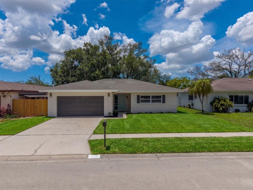 One or more photo(s) has been virtually staged. Welcome to this newly listed Beauty!  Have you been looking for an Updated, 3-way split home?  Well, here it is.  Walk into this lovely home and you will notice the wide-open feel of the living area with a beautiful fireplace and then you have the wide-open kitchen with quartz countertops and backsplash, cabinets are the newer style slim Shaker Cabinets, Brand-new Stainless-Steel Appliance Package and a large 
Island with lots of storage.  This kitchen is definitely a Chef's delight, and you will never feel left out when entertaining as it overlooks the living area.  Dining area/Family room are to the left of kitchen.  Master bedroom with its own remodeled ensuite is off the living area.  If you don't like sharing your sink you don't have to as there are two!  Master has 2 closets also.  To the back of the house is another good size bedroom and a remodeled bathroom and in the hallway, you have your very own inside laundry area. On the other side of the house off the dining area is the 3rd bedroom for the utmost of privacy.  There is also an oversized 2 car garage.  The backyard is lovely with a deck for relaxing on and looks at the little creek.  Everything is New or Newer.  Roof 1/26, AC, Electrical and so on and the best part - This is in a non-evac flood zone and close to Pinellas Park High!
Virtual photo of front yard with grass. Seller is installing sod.