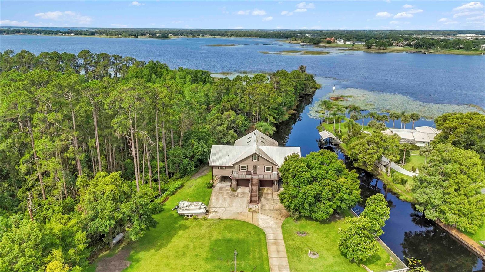 This stunning Elevated Lakefront home is a RARE find. Perfectly situated on Lake Lizzie with Conservation area on one side and Waterfront on the other. This 5-bedroom, 3-bathroom home invites Relaxation and Comfort. Enter from the stairs leading to the front door of this Completely Remodeled one-of-a-kind home and walk through the Entryway that leads into an open concept kitchen, dining and living area with vaulted wood ceilings and a Large Stone Wood Burning Fireplace. The area is light and bright with skylights and double French doors, with Hunter-Douglas (2019/2020) remote powered shades on the upper level. The Chef’s kitchen is well appointed, including quartz countertops, ceramic farmhouse sink, GE (‘Café’) double ovens, microwave, 5 burner gas stovetop and hood, Tru cabinets, Bosch dishwasher and built in pot filler. After dinner, relax and enjoy the sunsets and wildlife, on the large newly screened in porch. There are additional lake views on the unscreened decks with sliding glass doors off the dining area and the master suite. Take the spiral staircase to the In-Law apartment, complete with it’s own full-sized kitchen and bath. The apartment has it’s own Newly Screened Porch with a Large Swim Spa installed in 2021, West facing on the lake. The entire home is set up for Home Automation. The most recent Upgrades to the home include Metal Roof, Front Door, Attic Insulation for Energy Efficiency, Rebuilt Seawall, Fencing, Fire Pit. There is also a Generac 24kW generator installed in 2017 that seamlessly keeps power on throughout the home. There is a Community Boat Ramp Conveniently located adjacent to the property.