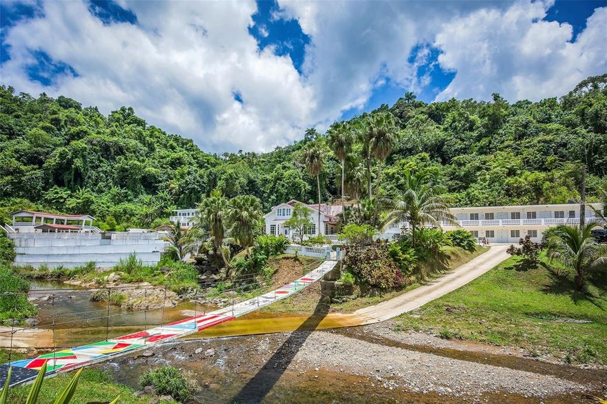 Discover an exceptional opportunity to own a one-of-a-kind mountain estate in the heart of Puerto Rico’s lush central highlands. Nestled within 23 acres of rolling terrain, this expansive property offers unmatched privacy, panoramic mountain views, and an atmosphere of pure tranquility, making it the ideal setting for a boutique wellness retreat, nature-inspired hospitality project, healing sanctuary, or an exclusive private estate.
 
Strategically located just 40 minutes from Ponce, one hour from Arecibo, and 90 minutes from San Juan, the estate provides the perfect balance of seclusion and accessibility. Guests and visitors will enjoy a peaceful escape without sacrificing proximity to major cities, airports, and coastal destinations.

Whether you envision a sanctuary for healing and reconnection, a private luxury compound, or an income-producing tourism venture, this property is uniquely positioned to support a visionary project that honors the natural surroundings and meets the growing demand for experiential travel.

The estate comprises five buildings, three of which are dedicated residential structures. At the heart of the property is a stunning two-story main house, beautifully crafted in wood and featuring multiple bedrooms, bathrooms, and a private kitchen. Two additional guest residences complement the main home, bringing the total to 19 fully furnished bedrooms thoughtfully distributed across the property. Collectively, the residential buildings offer approximately 12,440 square feet of interior living space, providing ample accommodations ideal for retreats, family gatherings, or group getaways.

At the heart of the outdoor amenities lies a striking 35 ft. x 55 ft. swimming pool, with a capacity of roughly 100,000 gallons, perfectly positioned to capture breathtaking mountain views and the nearby river. Enhancing the poolside experience is a dedicated kitchen building designed for seamless outdoor dining and entertaining. Above, an open-concept balcony serves as a picturesque venue for events, offering elevated panoramic vistas of the surrounding landscape.

Recreation and wellness amenities include a separate building with a game room and a fully equipped gym, featuring 18 workout machines. An efficient commercial-grade kitchen is also on-site, ideal for hosting meals or catering events. In total, the square footage of all buildings—including residential, recreational, and amenity structures—exceeds 20,000 square feet.

The grounds are dotted with charming walking paths and footbridges that cross the river running through the estate. Nearby attractions include Lago Garzas, Bosque Estatal de Guilarte, and Cascada Las Garzas, placing you in close proximity to some of the island’s most scenic natural areas.

Additional property features include a 30KW backup generator, a 5K water cistern, and the inclusion of all furnishings, appliances, and fixtures, making this an expansive and well-equipped estate ready for immediate use.