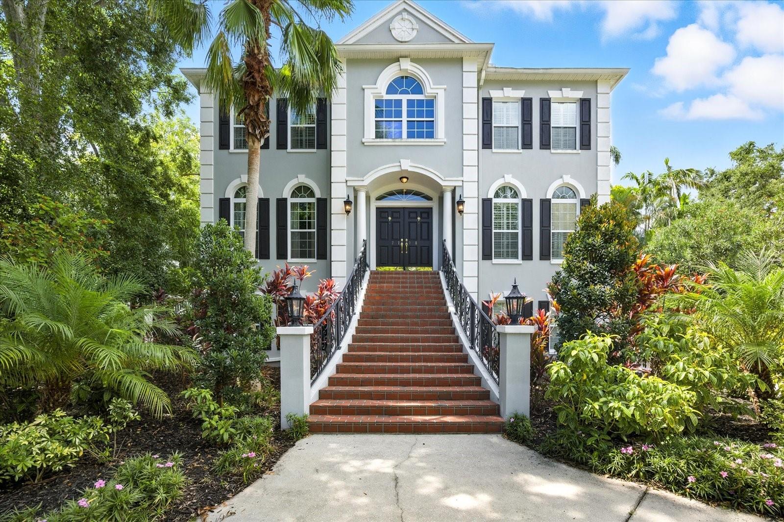 Step into timeless elegance in this breathtaking estate that evokes the grandeur of a southern mansion in the city. This exquisite BLOCK HOME is perfectly situated on a lush, private, tropical oasis. Incredible OVERSIZED LOT boasting over 15,000 sq ft of beautifully maintained gardens, private pond, 2 fountains, and gorgeous landscaping. This 4220sf residence is filled with natural light and beautiful upgrades and is the perfect place to call home. Talk about making an entrance...starting from the circular driveway, you are welcomed by a custom iron railing leading up to a magnificent foyer adorned with gleaming marble floors and a sweeping staircase that will set the tone for refined living. The traditional floorplan includes 4 bedrooms with the option to convert office as a 5th bedroom, a formal living room and formal dining room with wainscoting, & wood paneled office on the 2nd level is complete with closet and FULL BATH. Open concept family room/kitchen with dine-in breakfast nook, all adorned with immaculate Rosewood wood flooring & crown molding, exuding warmth and sophistication. Primary en-suite includes dual vanities, walk in shower with 2 shower heads, 2 large walk-in closets with custom shelving & a third closet with key lock for valuables. All bedrooms include plantation shutters and/or beautiful decorator window treatments.
The inviting family room features a gas fireplace framed by custom-built bookcases and three sets of french doors overlooking this spectacular nature preserve in the city. Enjoy serene views of the man-made pond with sparkling fountain sitting on your covered balcony. This balcony spans the width of the home and serves as a tranquil extension of the living area which is perfect for entertaining or quiet relaxation.
The chef’s kitchen boasts an oversized walk-in pantry, double oven, breakfast bar, gas stove and ample counter space. PRIVATE ELEVATOR services all 3 floors. Also included; generator, two A/C units, 2 gas water heaters, OVERSIZED side-entry 3 car garage, hookup for water softener, rain barrel, and ground level BONUS ROOMS that can be used as a game room, art studio, or media room. The garage is complete with built in storage cabinets and workbench. This extraordinary property combines classic architecture with tropical tranquility—a rare find offering both grandeur and privacy steps from Bayshore Blvd.