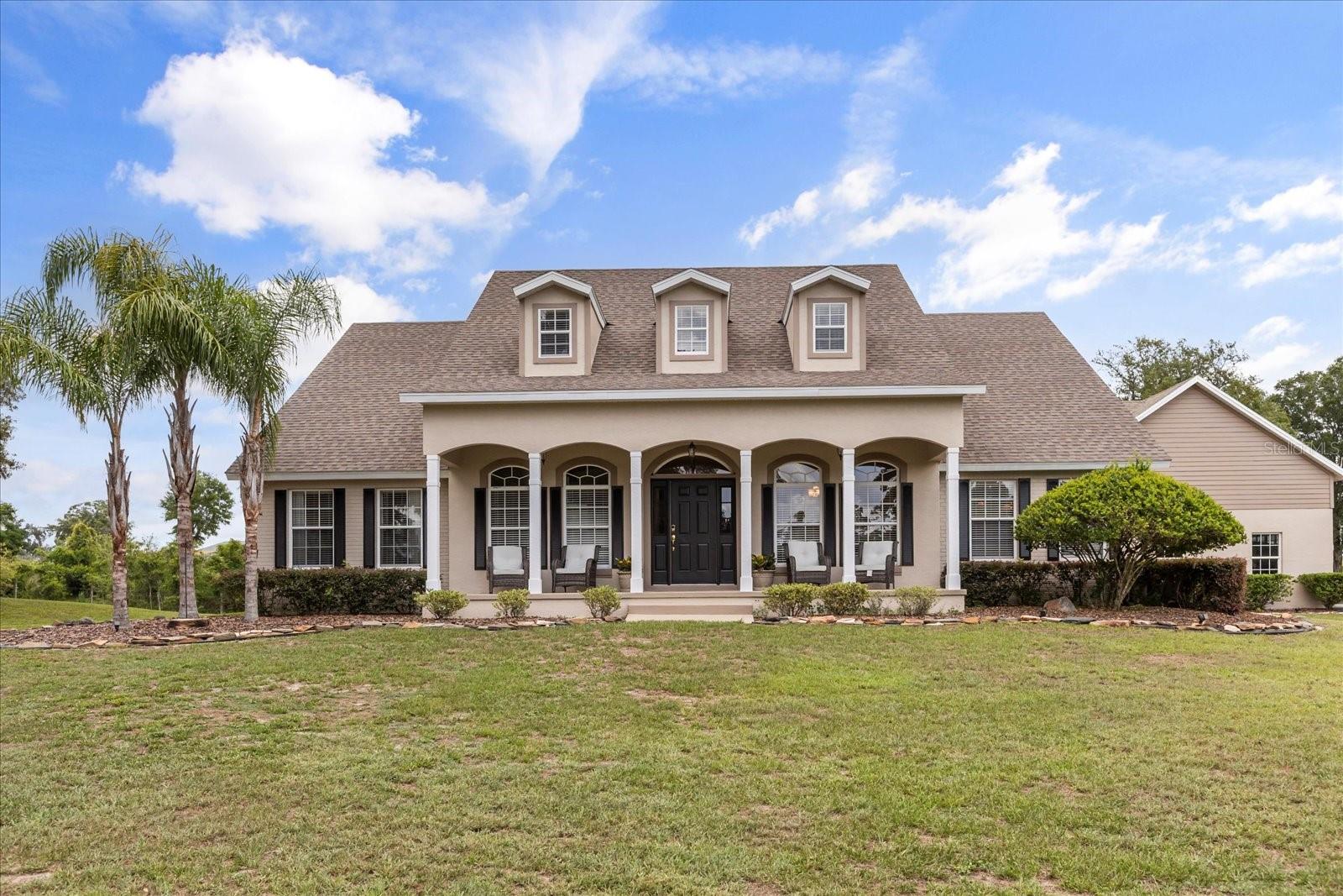 This stunning property offers serene country living while being conveniently located just 15 minutes from downtown DeLand, where you’ll find a variety of unique shops and restaurants. The 4 bedroom, 3.5 bathroom home sits on 5 acres, featuring two fully fenced pastures zoned for cows and horses, making it an equestrian lover’s dream. A long, paved driveway leads to the house, where mature oak trees and a charming covered front porch provide a warm welcome. You’ll find beautiful wood floors and tile throughout the main floor, complemented by high ceilings and an abundance of natural light. The living room features double French doors that open to a large covered back porch and a cozy wood burning fireplace, creating a perfect space for relaxation and gatherings. The kitchen, situated off the dining and living areas, includes a breakfast bar and a separate dining nook for informal dining. There’s also a dedicated office/den space off the front entrance. This home is perfect for entertaining, with spacious living areas and seamless indoor outdoor flow. The primary suite is located on the main floor with his and her closets, double vanities, and a dedicated makeup vanity. Upstairs, there are two additional bedrooms and a large bonus room—perfect as a playroom, entertainment space, or guest retreat. The exterior of the home was freshly painted in 2025, and the driveway was repaved in 2023. Additional updates include high-efficiency A/C units installed in 2024 and a new roof installed in 2018. The 960 sq. ft. three car garage features shark coated flooring for easy maintenance, cabinets for storage, and a 2024 installed mini-split unit, making it ideal for a gym, workshop, or gathering space. The garage also has a separate 150 amp panel separate from the main home and 700 sq. ft. of storage space above that could be converted into additional living quarters. Completing the property is a 1,000 sq. ft. barn with two stalls, a tack room, and a workshop. Whether you’re seeking a family home, a hobby farm, or a personal retreat, this property delivers in every aspect.