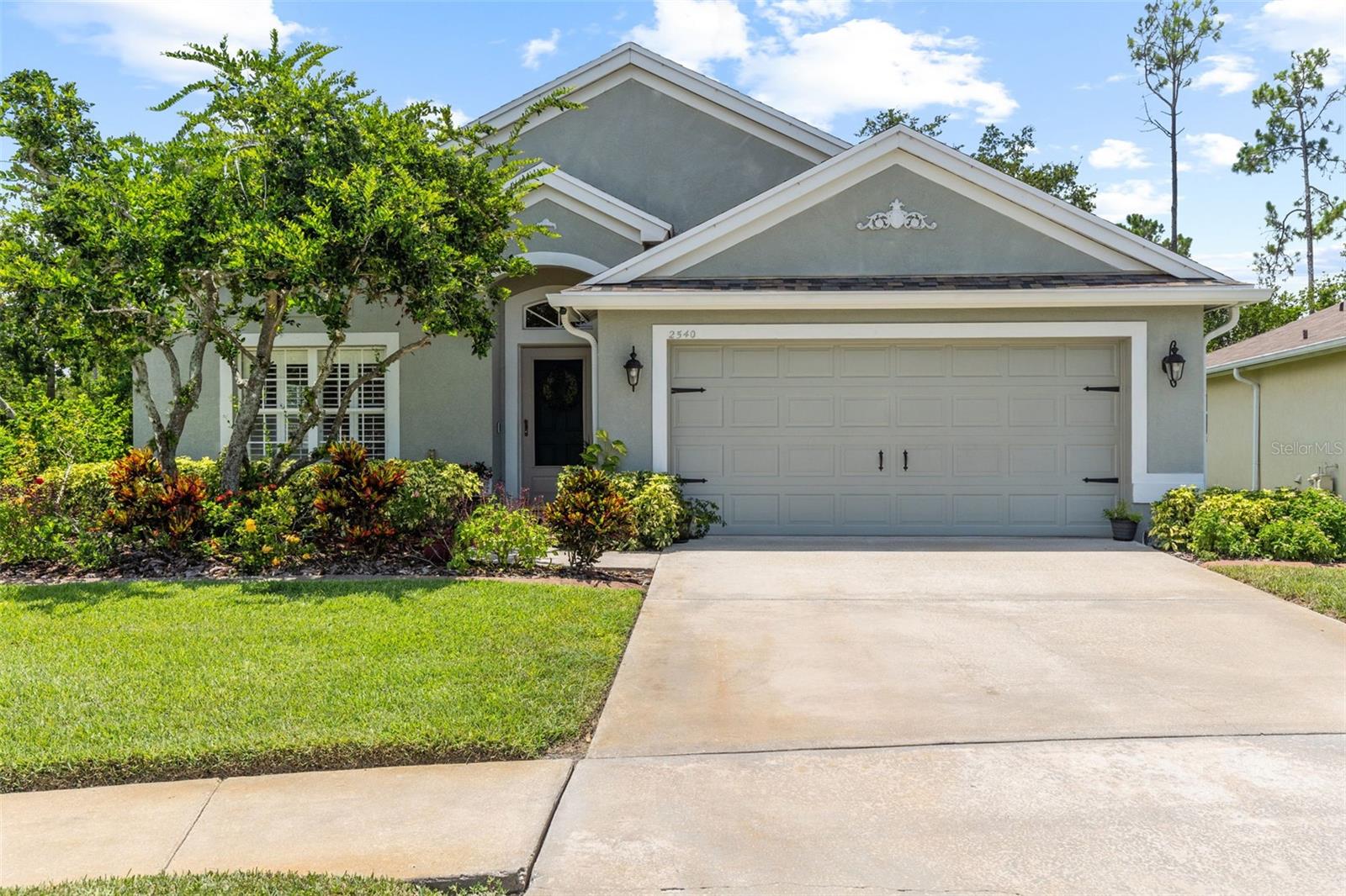 One or more photo(s) has been virtually staged. Poised in the sought-after gated community of Seven Oaks, this thoughtfully designed 4-bedroom, 2-bath, 2-car garage pool home offers a harmonious blend of comfort, style, and functionality. The curb appeal is undeniable with beautifully manicured landscaping and a covered entryway that sets the tone for what awaits inside. As you step through the front door, natural light floods the space, drawing attention to the elegant architectural archways and stately columns that define the first living area. Vaulted ceilings, recessed lighting, plantation shutters, and rich laminate flooring add warmth and sophistication, making this the perfect space to gather or relax. Just beyond the archway lies the heart of the home: an open kitchen designed to inspire. Featuring granite countertops, stainless steel appliances, a built-in desk, eat-in kitchen space, and a generous closet pantry, this culinary space offers both beauty and functionality. Recessed lighting highlights every thoughtful detail, while views of the backyard retreat invite seamless indoor-outdoor living. Adjacent to the kitchen is a spacious laundry room complete with shelving and a storage closet, offering everyday convenience. Continue into the secondary living area—bathed in natural light thanks to expansive sliding glass doors that frame views of the pool area and tropical landscaping. The large primary suite is a serene retreat tucked just off the main living space, offering private sliding door access to the outdoor area, a spacious walk-in closet, and a spa-inspired en-suite bath. You'll love the dual sink granite vanity, modern fixtures, luxurious garden tub, and glass-enclosed shower with a stone-tiled floor. Bedrooms two, three, and four are thoughtfully positioned to maximize privacy and space, each offering ample closets and ceiling fans. The second full bathroom continues the modern aesthetic with granite countertops and updated finishes. Step outside to a breathtaking outdoor escape—your personal resort-style haven. A covered patio and screened lanai provide the perfect backdrop for entertaining or unwinding. The sparkling blue pool is enhanced by a tranquil water feature, outdoor shower, integrated lighting, and wired speakers. Surrounded by lush tropical landscaping, this space offers true Florida living at its finest. Additional upgrades include: Roof (2020), AC (2023), Refrigerator (2024), and Dishwasher, Disposal, Microwave (2020). Beyond the home, the Seven Oaks community offers an array of resort-style amenities. Enjoy the sun deck with private cabanas, swim in the Junior-Olympic lap pool with a thrilling double-loop waterslide, or let the splash park bring out your inner child. Sports enthusiasts will appreciate the tennis courts, sand volleyball court, softball and soccer fields, and a fully-lit basketball court. The welcoming clubhouse features a fitness center, locker rooms with showers, a multi-tiered theater with a projection screen, gathering spaces, and a café for your convenience. Located near top-tier shopping and dining options like The Shops at Wiregrass, Tampa Premium Outlets, you'll have everything you need just moments away. With premier medical facilities such as Advent Health of Wesley Chapel and BayCare-Wesley Chapel. This isn’t just a house—it’s a place to call home. Schedule your private tour today and discover the comfort and lifestyle that await you in Seven Oaks. For a virtual tour, click the provided link.
