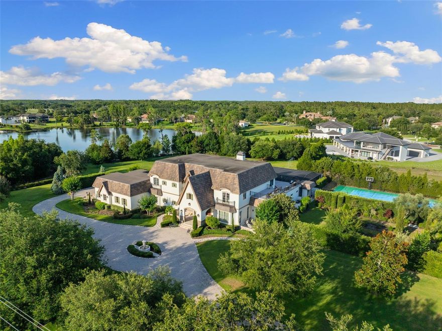 Welcome to 18521 Wayne Road — a gated luxury estate boasting nearly 10,000 square feet of living space and almost 15,000 under roof on 4.75 acres, complete with lake views, manicured grounds, privacy hedging, and resort-style amenities. Offered for the first time, this custom-built architectural masterpiece blends elegant design, smart home technology, and modern convenience. The residence includes 6 bedrooms, 7 full bathrooms, 1 half bath, two stories, and an elevator for seamless access. A Control4 system manages lighting, audio, security, and climate, with zoned thermostats in each bedroom and Anderson double-pane windows throughout. Enter through a private gate leading to a circular drive with a fountain, surrounded by lush landscaping and striking curb appeal. Outdoor highlights include a perennial garden, tennis/basketball court, fruit trees, firepit, and a 1,319 sq ft second-story balcony. An 8-car garage with tandem bays and a utility garage offers ample space for a car collection. Inside, a grand foyer with chandelier, spiral staircase, and stone and marble flooring sets the tone. The heart of the home is the expansive family room and kitchen—ideal for entertaining. The family room features soaring ceilings and French doors opening to the 1,169 sq ft covered lanai and pool area. The chef’s kitchen is both elegant and functional, anchored by a large island and outfitted with a built-in Meile coffee system, Viking double ovens, gas cooktop beneath a stone range hood, double dishwashers, double microwaves, pot filler, two sinks, under-cabinet lighting, and cabinet garage. A hidden walk-in pantry includes extra refrigeration and storage, while a nearby wine cellar adds sophistication. Enjoy courtyard views from the kitchen, along with a breakfast nook and a formal dining room ideal for gatherings. The left wing features an entertainment room with bar, pool table area, private movie theater, and two bonus rooms currently used as a gym and art studio. Sliders open to the covered lanai with an outdoor kitchen, gas fireplace, and floating TV—perfect for indoor-outdoor living. Tucked away is a maids’ quarters with guest bedroom and en-suite bath, ideal for live-in staff or extended stays. Nearby, a large laundry room includes two washers, two dryers, and built-in cabinetry. The right wing features a formal living room with fireplace, executive office with private loggia, and a luxurious primary suite with tray ceilings, fireplace, wet bar, lanai access, and spa-style bath with jacuzzi tub, walk-in shower, and dual walk-in closets—one with center island. Upstairs, accessible by elevator or two staircases, are four additional bedrooms with en-suite baths, plus a loft with built-in desk and reading nook. A spacious bonus room includes a walk-in closet, wet bar with mini fridge and microwave, and access to the second-floor balcony—perfect as a game room or flex space. Step into your private backyard oasis: a 60,000-gallon saltwater pool with rock wall, waterslide, 12-person jacuzzi, charming bridge, and in-floor cleaning system. An outdoor shower and extra storage complete the space. Additional features include a whole-house 48kW generator, three new water heaters, a 1,000-gallon buried propane tank, five zoned HVAC systems, invisible fence, and generous storage throughout. Complete with a private dock, security system, and luxury amenities, this is an exclusive opportunity to own a landmark Odessa estate.