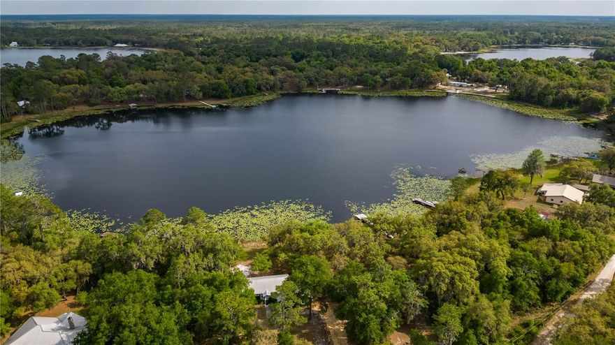 Breezy waterfront living never provided so much potential! Overlooking the sparkling spring-fed Miles Kale Lake in the quiet area of Fort McCoy, this property offers a total of three parcels that each feature roughly 100 ft. of shoreline and a combined 1.91 acres. All of the acreage is fenced, and 2 residences rest on two of the parcels, with the third lot being left in a more natural state as a lovely heavily wooded area. Move-in ready, both homes have been lovingly maintained and are move-in ready with full furnishing. Used currently as VRBO, there is ample potential to continue this usage without much fuss or to instead use this as a personal vacation compound or as year-round residence with a designated guest, in-law, or rental home. On the northern lot is the home named The Big Green House– offering a total of 2-bedrooms and 2-baths, the home was meticulously rebuilt and expanded with all new plumbing, electrical wiring, trusses, a standing seam metal roof, and is highly energy efficient. The interiors feature ample natural light, tall vaulted ceilings, beautiful tongue-and-groove wood work throughout, and lots of space to enjoy. The home features a large great room, as well as a large open kitchen that includes stainless steel appliances, abundant counter and cabinet space, center island with breakfast bar, and adjacent dining nook. Both bathrooms are immaculate, with recent updates and a clean aesthetic. A large screen-enclosed porch rests to the back of the home, providing a wonderful space to enjoy stunning views of the lake and a cozy area to catch some shade. The secondary residence, called The Brown Cottage, rests on the center-most lot. Offering 1-bedroom and 1-bath, this charming cottage features a large family room, a delightful kitchen with adjacent dining area, and a great screen-enclosed porch that overlooks the lake. This home shares the rustic aesthetic of the green home, with lots of tasteful wood-work done throughout the home. A laundry shed is also attached to the home for added ease. Both residences share a well and pump, however, an additional well and pump could be added by the future buyer if desired. A private boat ramp with a recently updated dock allows for easy enjoyment of the lake, opening up a variety of uses for those who enjoy spending time on their boat. Mile Kale Lake is a wonderful, natural Florida lake with a nice sand bottom and a few unique features that make it extra exciting– the lake has a gradual slope and is deeper than many other lakes in the area. The lake is great for boating on canoes, kayaks, jet skis, or even power boats with other boats rarely being seen on the lake to provide little to no disruption on most days. Many other lakes are also in the area, making this an ideal property for those looking to discover the many options Central Florida has to offer! If you’re ready to take in pristine water-front views or are looking for an income producing opportunity, this property is a wonderful option to consider!