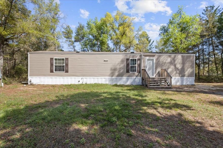 Built in 2022 and well maintained by its original owner, this manufactured home offers a bright, open floor plan with seamless sightlines from the kitchen to the living area. The kitchen has been thoughtfully upgraded with additional real wood cabinetry, including a convenient pull-out spice rack for enhanced storage. Just off the kitchen, the laundry area also features newly added wood cabinetry for added functionality.
The split-bedroom layout provides privacy, with the primary suite located on the left side of the home and featuring a private en-suite bath, while the secondary bedroom and bathroom are situated on the opposite side.
Set on a .24-acre lot with RV hook up, the partially fenced yard offers outdoor charm and versatility, highlighted by a decorative pond in the front yard, plus a garden shed and fire pit in the backyard—ideal for relaxing or entertaining. Located in the heart of Levy County, this home places you close to an abundance of freshwater springs, the Gulf and outdoor recreation, while still enjoying easy access to Gainesville and Ocala, both approximately 30 minutes away.