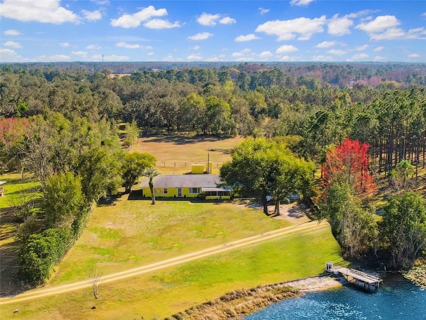 One or more photo(s) has been virtually staged. Experience true Florida lakefront living on this private 2-acre estate in Groveland with limited neighbors, offering 182 feet of pristine lake frontage, private dock, and direct boating access on a scenic fishing lake. Up to 1% lender contribution toward buyer closing costs may be available for accepted offers by February 28, 2026 when using seller’s preferred lender. Buyer must qualify. Limitations, terms, and conditions apply.

The 3-bedroom, 3-bath home spans just under 2,000 square feet and features a thoughtfully designed split floor plan with extra-wide hallways, multiple entrances into the home, and one entrance equipped with a small ramp for wheelchair accessibility, plus new expansive windows that capture stunning water views from the living room and primary suite. A screened-in front porch provides the perfect place to relax and enjoy peaceful lake breezes. The oversized primary suite offers a flexible sitting area, remote-controlled drapes, a convenient kitchenette with microwave, mini-fridge, and cabinetry, plus a spa-inspired bath with Jacuzzi tub and separate walk-in shower.

Additional interior highlights include a sunken Florida room with stone chimney and wood-burning fireplace, classic terrazzo flooring throughout much of the home, and a large interior utility/laundry room with shower and toilet—ideal for guests or outdoor use.

Recent upgrades provide peace of mind, including a new roof (2023), 5-ton A/C system (2020), newer water heater, new washer and dryer, and an updated security system with wired video and audio. The home is supplied by a clean natural aquifer water source, providing exceptionally pure water with no filtration or purification system required. 

Outdoors, the property truly shines with mature fruit trees, brick BBQ pit, fully fenced grounds, RV parking with 50-amp hookup, trailer hookup, generator hookup (generator not included), and multiple outdoor structures with electricity, including: a detached office/studio, a large metal Quonset-style building designed to withstand extreme wind speeds, multiple storage sheds, a golf cart shed, and a detached 2-car garage with attached shed. (Detached structures not included in living square footage.)

Tucked away for privacy yet conveniently located near town, this property delivers the perfect blend of tranquility, space, and functionality. With only three homes on the lake and expansive usable acreage, this is a rare opportunity to own a versatile lakefront retreat offering privacy, space, and endless possibilities.