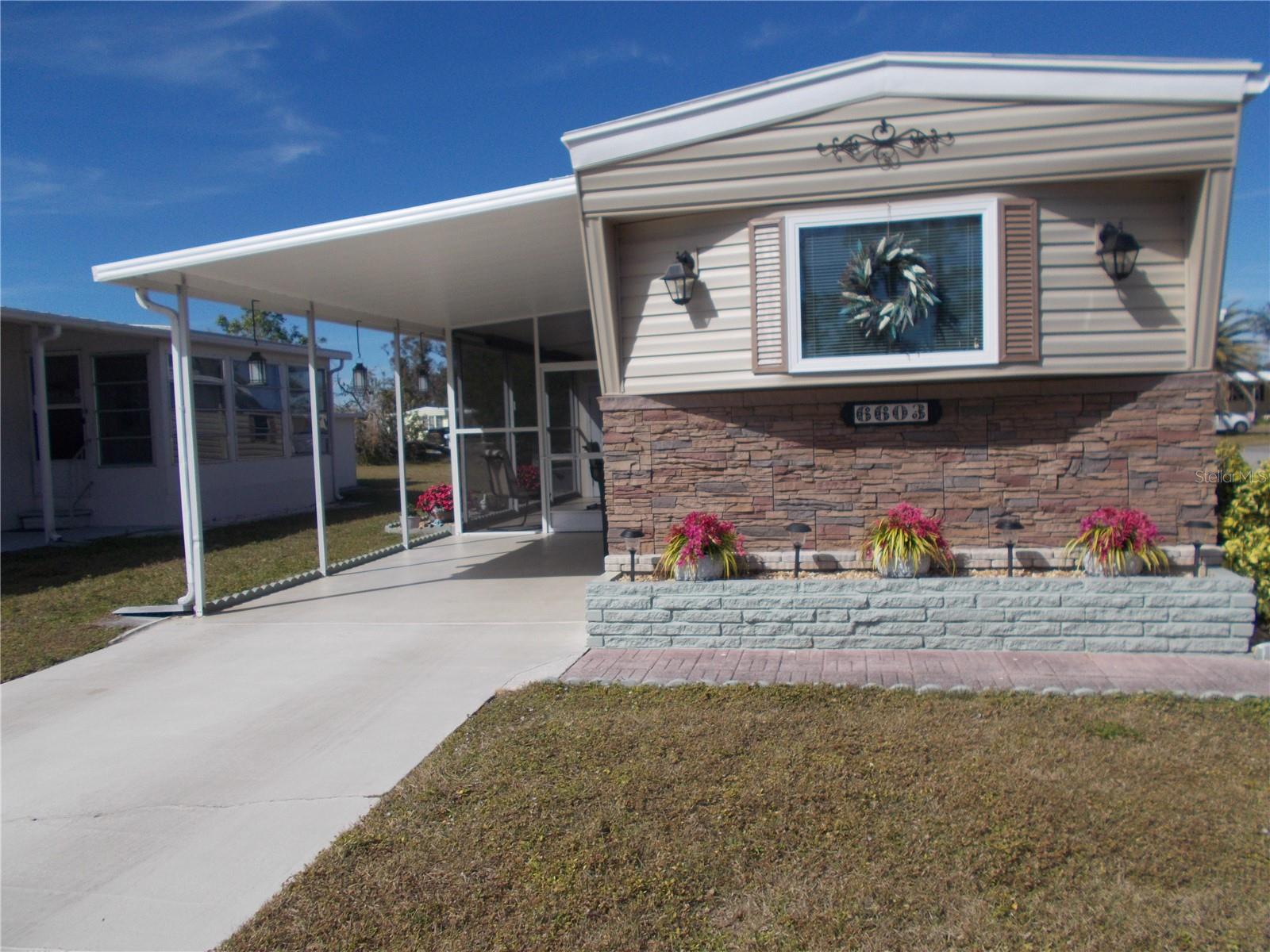 Welcome to 6603 Hauli Court where the curb appeal says it all. This is a nicely landscaped, corner unit with lovely GenStone brick siding, as well as vinyl siding. It is an Partially furnished 2 bedroom, 2 bath home in the 55+ Gated Mobile Home Community of Holiday Park. It is NOT IN THE PET SECTION. This home features a split floor plan and numerous updates. As per owner, new roof in 2020, AC in 2022 and laminate floors in 2018. New interior doors and new windows throughout the house. New countertop and sink in the kitchen and the Refrigerator and stove are from 2016. Washer and Dryer that are in the first shed (6X10) are from 2020. The second shed (6X8)is from 2020. You also have a very large Florida Room as well as a lanai for all your entertaining needs. In Holiday Park you own the land with a deed and your $195.00 monthly maintenance fee ($2340.00 a year) is included in your taxes. The community features 2 clubhouses, 2 swimming pools, a library, a fitness room, tennis courts, pickleball & bocce courts, to name a few. You are close to shopping, dining, entertainment, numerous golf courses, sports facilities, and SW Florida's renowned beaches. Come take a look!