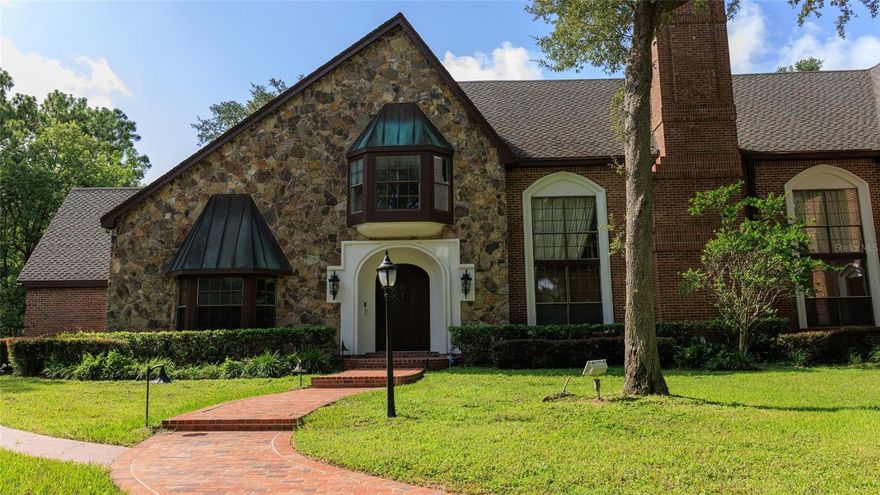 A Private European Estate in the Heart of Longwood!! Hidden beyond iron gates and a winding brick drive shaded by timeless-old oaks, this 5.13-acre estate emerges with quiet authority — a residence designed not to follow trends, but to transcend them. Spanning more than 7,600 square feet, the architecture draws inspiration from European manor homes, where craftsmanship was paramount and every detail carried intention. Stone and brick façades, carved columns, arched passageways, exposed beams, and rich custom millwork create a sense of permanence rarely found in contemporary construction. Inside, the grand two-story salon commands attention. Soaring ceilings, dramatic wood paneling, statement fireplaces, and sculptural staircases create an atmosphere both cinematic and intimate. Light filters through expansive windows, illuminating spaces designed for formal entertaining and private retreat alike. The chef’s kitchen is scaled for gathering — expansive granite surfaces, custom cabinetry, oversized islands, and seamless flow into formal and casual dining spaces. A secondary kitchen offers flexibility for hosting at scale, private staff accommodations, or multi-generational living. Five bedrooms and seven-and-a-half baths provide refined privacy. The primary suite is a sanctuary of architectural drama, featuring vaulted ceilings, a lofted sitting retreat, spa-caliber bath, soaking tub, and walk-in shower — a space designed for restoration as much as repose. Beyond the interiors, the estate transforms into a secluded resort. A screened courtyard pool anchors the home’s entertaining wing, creating year-round indoor-outdoor living. Meandering paths lead to a private tennis court, a tranquil pond with fire feature, and a romantic garden gazebo framed by statuary and lush greenery — a setting reminiscent of a European villa garden. An expansive motor court and multiple garage bays accommodate collectors and connoisseurs alike, offering exceptional space for automobiles, hobbies, or curated storage. Set within minutes of Central Florida’s conveniences yet worlds apart in privacy and character, this property represents a rare opportunity: Not merely a home — but a statement of individuality. Not merely acreage — but a private compound. Not merely architecture — but enduring presence. For the buyer who seeks something irreplaceable. Schedule your private showing today!