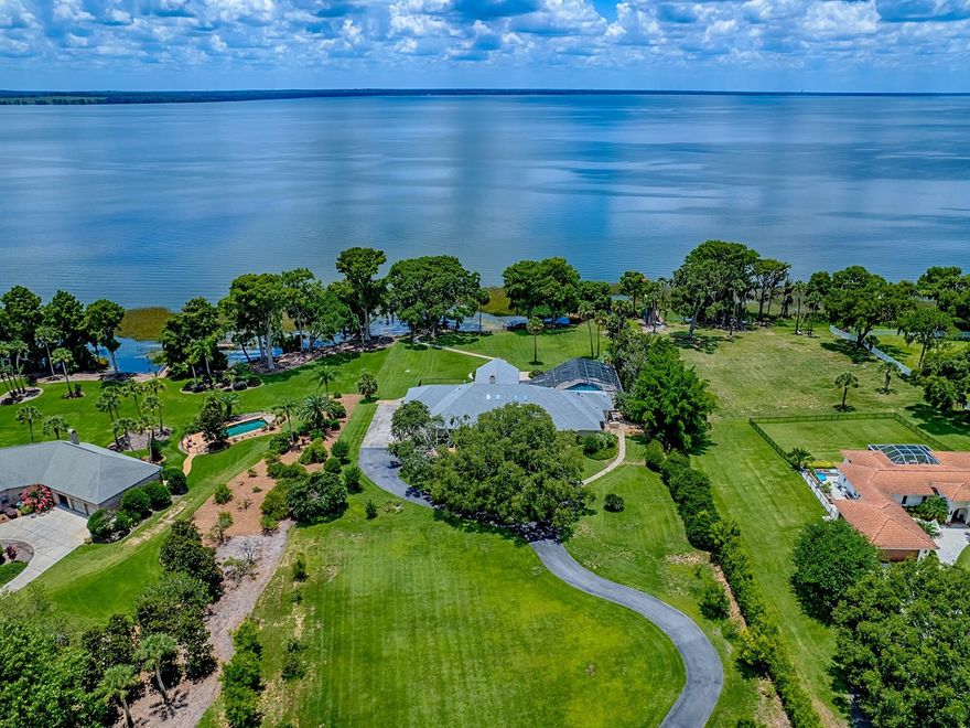 EXQUISITE WATERFRONT ESTATE ON HARRIS CHAIN OF LAKES - FLORIDA LUXURY LIVING AT ITS FINEST!

Welcome to this stunning 4-bedroom, 4.5-bathroom waterfront home, perfectly nestled on 5.78 private acres overlooking Lake Harris. With the rear of the home facing west, this home provides some of the most beautiful sunset views in Lake County nearly every evening! Boasting 5,900 sq. ft. of luxurious living space and an expansive 4,307 sq. ft. screened-in area, this property offers unmatched comfort and elegance. An attached oversized 2-car garage and a dedicated home theater add further appeal to this magnificent residence.

Entering through a private gated entrance, you are greeted by a picturesque, tree-lined drive under a breathtaking canopy of majestic oaks. The home, constructed with durable, cedar siding and refined stone accents, is an architectural masterpiece.

Step into the awe-inspiring foyer and experience the home's warmth and sophistication, highlighted by custom woodwork, soaring beamed ceilings, and a dramatic floor-to-ceiling stone fireplace in the formal living and dining areas. The spacious gourmet kitchen seamlessly flows into the expansive great room, offering spectacular panoramic lake views.

The master suite is nothing short of extraordinary, featuring a cozy sitting area with fireplace, lavishly appointed dressing spaces within expansive custom walk-in closets, dual vanities, separate water closets, a luxurious double-headed walk-in shower, and a tranquil soaking tub. A private, air-conditioned exercise room off the master provides a serene space for morning routines.

Throughout the home, thoughtful artistic touches and custom built-ins showcase unique craftsmanship and abundant storage options. Almost every room highlights magnificent views of the pool area and serene Lake Harris.

Step outside to your recently resurfaced saltwater pool and spa, surrounded by an elegant new paver deck, providing the perfect backdrop for entertaining and relaxing while enjoying breathtaking sunsets.

Additionally, this estate includes a detached guest home featuring a spacious 1-bedroom, 1-bath apartment with a balcony, its own 2-car garage, and a generous workshop/storage area. A 40x60-foot covered RV port equipped with three 50-amp connections adds exceptional convenience for your recreational vehicles.

Experience lakeside luxury living at its best—your private paradise awaits!