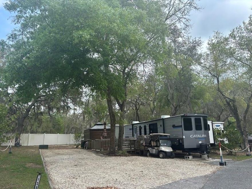 Large deeded rv Lot – Full time or Part time – This Lot features one of the most spacious lots in the resort while backing up to the common area / fence. Deck already in place to keep the sand and dirt away! Enjoy the evenings on the deck or in the gazebo watching tv. Small dog area already established -Metal shed has washer & dryer for your needs - Shade is provided throughout the resort with large oaks and hickory trees adorned with Spanish moss that dances in the breeze. Sand hill cranes wander about. Your canoe is at hand for an early morning fishing trip along the shoreline or take the kayak if you prefer. For the boaters you may take an afternoon slow cruise around the lake. Glorious sunsets will prompt oohs and aahs from your visitors or friends as the sunsets are breath taking. Come enjoy all the amenities of the park which include a clubhouse, 2 swimming pools, tennis court & shuffleboard, to name a few. Centrally located to Ocala, Palatka and only hour or so from Daytona Beach! Your golf cart will get you to the nearby stores and post office. Your electric bike will propel you around the paved streets of the resort – for the more adventurous grab the mountain bike and enjoy all the nearby trails. The 2023 Catalina RV unit will remain on the property and will be between the Sellers & Buyer(s).
