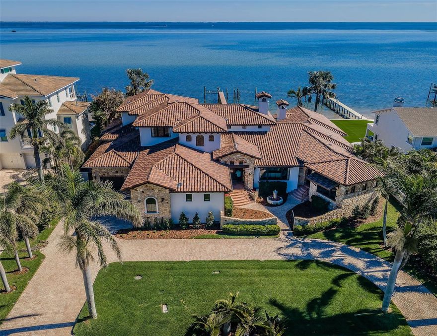THIS SPRAWLING CUSTOM COASTAL TUSCAN ESTATE DELIVERS A SPECTACULAR LIVING EXPERIENCE WITH UNFORGETTABLE OPEN WATER VIEWS OF TAMPA BAY!  A long, stately driveway with a wonderful grotto-like entry courtyard introduces a brilliant residence whose commanding presence tells your guests that you have arrived.  From custom groin & barrel-rounded ceilings, magnificent lighting and   splendid archways, to the smallest of opulent details that are felt and seen, you will find yourself immersed in the lap of luxury.  Exquisite hand-selected materials and world-class artisan quality craftsmanship define this masterful 6500sqft of living area.  Step into the 650sqft great room overlooking the waterfront; with 22ft-high beamed ceilings and a mammoth stone-finished gas fireplace, this remarkable space mirrors the great halls of yesteryear.  A stunning16ft-wide floor-to-ceiling brick and stone archway transitions to the sumptuous gourmet kitchen with custom designer cabinetry, single-slab ogee-edge granite counters, island prep center, separate island breakfast bar, Wolf gas double ovens, Subzero/Bosch appliances and sizable walk-in pantry – all to make your culinary experience a true joy.  Large waterfront living room is supported by an elegant wine/beverage center and a fabulous custom designer bath.  The owner’s wing boasts an exceptional executive office and a superb waterfront bedroom suite with 14ft-high vaulted beam ceilings, cast stone gas fireplace, and an incredible custom closet system with three built-in dressers.  Owner’s bath is an indulging, pampering retreat, with custom designer vanities, a generously-sized deluxe cosmetics center, a gorgeous built-in microjet spa tub, and a lavish dual-head walk-in shower finished in polished-stone.  Upstairs, discover a spacious family/game room and two luxurious guest bedrooms suites overlooking the bay.  Through a dedicated exterior entrance rests the guest house, with oversized bedroom, walk-in closet, posh beverage center and plush full bath.  Beyond the great room, discover the 640sqft covered outdoor cooking, dining and lounging area; overlooking the pool deck and Tampa Bay, and beautifully-appointed from top to bottom, you’ll love this amazing entertainment space.  The dazzling Pebbletec pool enjoys numerous water features, and a huge, separate 12-person hot tub – heated by gas or heat pump.  For those chilly nights, gather around the fine built-in gas firepit as you gaze at the lightshow across the bay.  Beyond the pool deck rests an open grassy area showcasing your 120ft of sweeping waterfrontage and miles of panoramic water views!  Backup generator, whole house water filtration/conditioning, Control4 whole house multi-media, mudroom, a terrific laundry facility, boat dock/lift and scores of features/amenities far too numerous to mention here.  By any measure, this is an astonishing legacy luxury estate!  Buyer to verify dimensions.