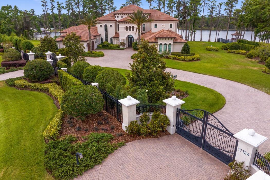 A rare opportunity to live expansively, privately, and beautifully- 17124 Crawley Road is a gated lakefront estate offering timeless design, modern comfort, and breathtaking natural surroundings. Built in 2017 and situated on the tranquil shores of Rainbow Lake with 300 feet of private frontage, this custom-built residence offers nearly 10,600 sq ft of total living space, including a 1-bedroom guest cabana. Set on 5.89 private acres, this estate is designed for both grand entertaining and everyday luxury - without HOA or CDD restrictions.
Key Features:
• GRAND ENTRY & LIVING SPACES – Enter through dramatic double doors into a soaring foyer with a dual staircase. The formal living room features 24-ft ceilings, gas fireplace, and panoramic views of the pool and lake. A comfortable family room with electric fireplace and sliding glass doors opens seamlessly to the outdoor terrace.
• DESIGNER KITCHEN – A Cianitus granite island anchors the space, complemented by Cambria Menai quartz countertops and designer chandeliers. Equipped with a gas range (1.5 ovens), wall oven, pot filler, microwave, refrigerator, and adjacent butler’s pantry with granite countertops and wine fridge. Flows into the formal dining room - ideal for gatherings large or small.
• PRIMARY SUITE & MAIN LEVEL ROOMS – The main-level primary suite includes a fireplace, sitting area, dual custom walk-in closets, and spa-inspired bath with freestanding tub and oversized walk-in shower. Two additional ensuite bedrooms, a soaring study, and dedicated gym complete the thoughtful main floor.
• UPSTAIRS LIVING – Two oversized suites upstairs, each with private baths and walk-in closets—perfect for guests, teens, or multigenerational living. The upstairs entertainment zone includes a sunken game room, wet bar with fridge, and balcony overlooking the serene lake and pool.
• PRIVATE GUEST CABANA – Located just off the pool, the 1-bedroom guest house features a full bath, walk-in closet, built-in TV, crown and tray ceilings, and a bar with refrigerator—ideal for extended stays or work-from-home space.
• RESORT-STYLE LIVING by Ryan Hughes Design Build – Heated saltwater pool and spa, fire pit, stacked stone retaining walls, covered terrace, full summer kitchen, and a separate outdoor bath. Lush gardens, fruit trees, mature landscaping, and paver walkways lead to the private dock- installed in 2021- with electrical and nautical rope detailing, offering direct access to Rainbow Lake.
• ADDITIONAL HIGHLIGHTS – Features 8-foot doors on both levels, two 2-car garages (one on each side), EV charging station, dual laundry rooms, custom-finished walk-in closets in every bedroom, and intricate crown and tray ceilings throughout.
• This estate is more than a home- it’s a retreat. Wake up to shimmering lake views, unwind in complete privacy, and enjoy the serenity of expansive natural surroundings. Whether you’re hosting, relaxing, or creating a legacy, this property is ideally suited for multigenerational living.
• Located in the heart of Odessa- one of the Tampa Bay area’s most sought-after communities for its natural beauty, larger homesites, and tranquil lifestyle- you’ll enjoy the peace of country-style living with the convenience of being just minutes from top-rated schools, hospitals, dining, shopping, major highways, and Tampa International Airport. It’s the perfect balance of space, serenity, and accessibility.