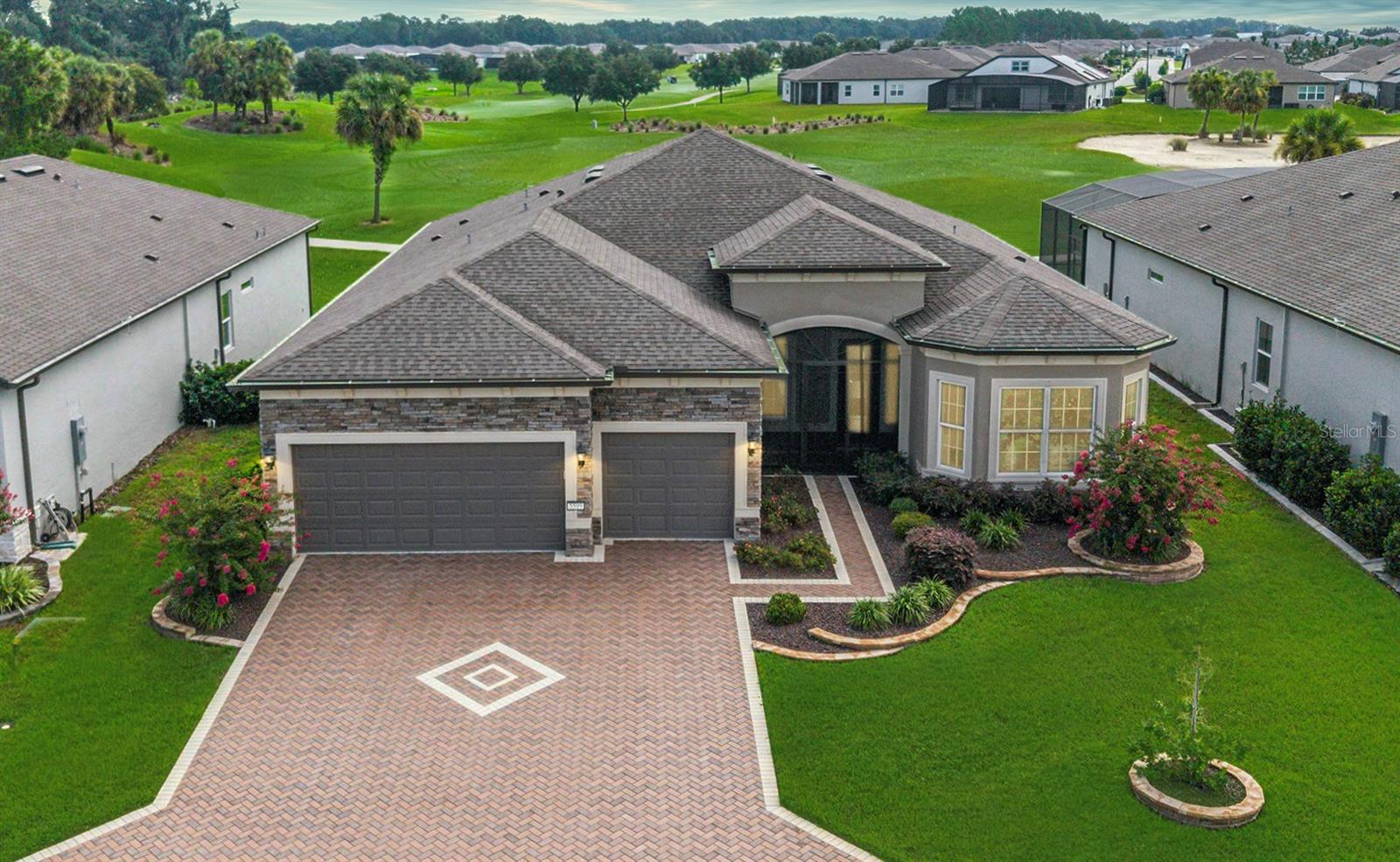 Refined Luxury Meets Unparalleled Golf Course Living! Immerse yourself in refined resort-style living with this nearly-new, masterfully curated Stellar model—boasting 3 bedrooms, 3 baths, a versatile flex room, and over $200,000 in premium upgrades. Gracefully positioned on a coveted golf course lot within the gated 55+ enclave of Stone Creek, this residence offers timeless architectural sophistication, exceptional craftsmanship, and sweeping panoramic views. From the moment you arrive, you’re greeted with distinguished curb appeal: meticulously designed landscaping, stacked stone accents, a herringbone-pattern paver driveway, and signature Craftsman-inspired elements. Step through the elegant glass-inset entry into a sweeping open-concept living space defined by 10’8” ceilings, motorized shades, luxurious porcelain tile flooring, and striking zero-corner glass sliders that blend seamlessly into the expansive outdoor sanctuary. Perfectly designed for both tranquil mornings and lavish entertaining, the extended covered lanai and 12’x22’ birdcage patio offer breathtaking golf course vistas. Inside, the gourmet kitchen serves as a focal point for culinary artistry, featuring 42” designer cabinetry crowned in molding, gleaming quartz surfaces, high-end built-in KitchenAid stainless steel appliances, and a stately wood canopy hood. A thoughtfully customized walk-in pantry and an oversized island with designer pendant fixtures complete the experience, while the adjacent built-in bar with wine refrigeration delivers effortless elegance for refined and effortless entertaining. The owner’s suite offers an upscale retreat with calming views, a tray ceiling embellished with crown molding, a shiplap accent wall, and statement chandelier lighting. Pamper yourself in a spa-inspired bath retreat featuring a comfort-height double vanity and a Roman-style walk-in shower enhanced by a striking glass tile inlay, transom window, and built-in seating for moments of relaxation. Completing the experience is a fully custom-designed walk-in closet, echoing the elegance of a luxury boutique while delivering seamless convenience and elevated style. Guests will enjoy exceptional privacy and comfort in the front bedroom, complete with a bay window and en suite bath, while the third bedroom invites flexibility for a hobby room, studio, or luxe office space. This home is pre-wired for a pool and full security system, and includes a state-of-the-art sound system, an expansive laundry suite with cabinetry and folding surface, and a thoughtfully placed mudroom leading to a 4’ extended three-car garage featuring epoxy-coated flooring, overhead storage, and room for a golf cart or workshop. Life at Stone Creek extends beyond the walls of this exquisite residence. Enjoy access to a vibrant and amenity-rich community—from championship golf and resort-style pools to a world-class health spa and a lifestyle department offering curated excursions, engaging entertainment, and enriching activities. This home is more than a place to live—it’s the ultimate expression of elevated living, where style, serenity, and social connection converge.