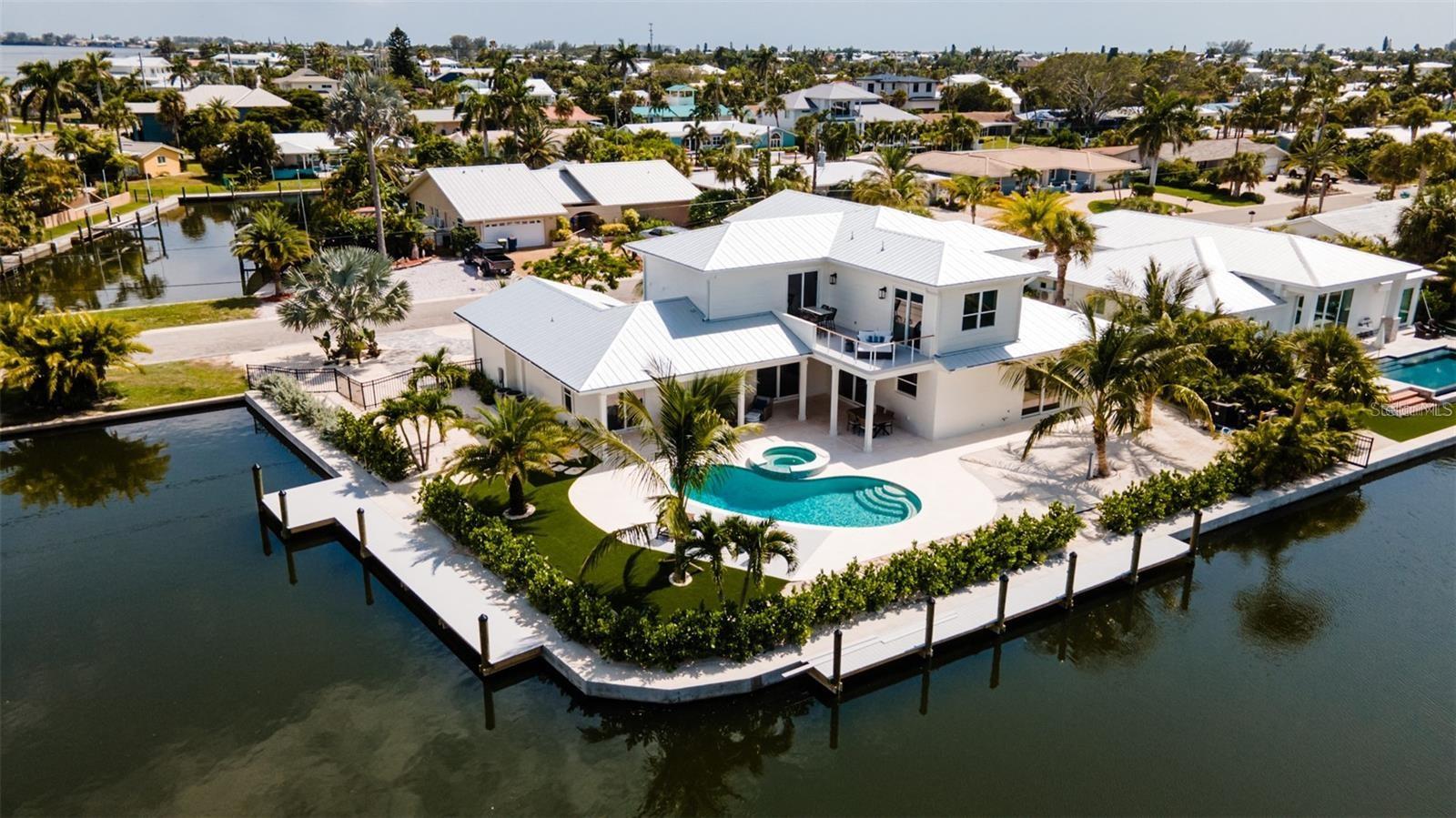 Stunning turnkey new construction on Anna Maria Island, located on a serene and rare double channel lot in the Key Royale neighborhood. This spacious residence features 5 bedrooms, 2 on the main level and 3 upstairs, all with en suite and walk-in closets offering ample space for family and guests. The main floor’s primary suite includes a large bathroom with steam shower and beautiful marble tile flooring. Enjoy 2 living spaces, one on the main level and another with a large balcony overlooking the canal on the second floor. The elevator provides easy access to both levels. Convenient laundry with 4 washers and 4 dryers, 2 upstairs and 2 on the main level. Upgraded finishes throughout with wide plank engineered walnut flooring, marble tile in the bathrooms, quartz countertops, 8' high extra thick upgraded doors, and upgraded trim package. The modern kitchen boasts brand new high-end Sub-Zero and Wolf paneled appliances and upgraded cabinetry. Step outside to enjoy covered seating and dining areas, a large saltwater pool and spa with breathtaking canal views, and 2 new composite wood docks with new seawall on this home's rare corner channel access, ideal for water enthusiasts. The property also features garage spaces to accommodate 4 vehicles, and new mature landscaping. The home's interiors are thoughtfully designed with hand-curated, beach inspired furnishings which are included in the sale.