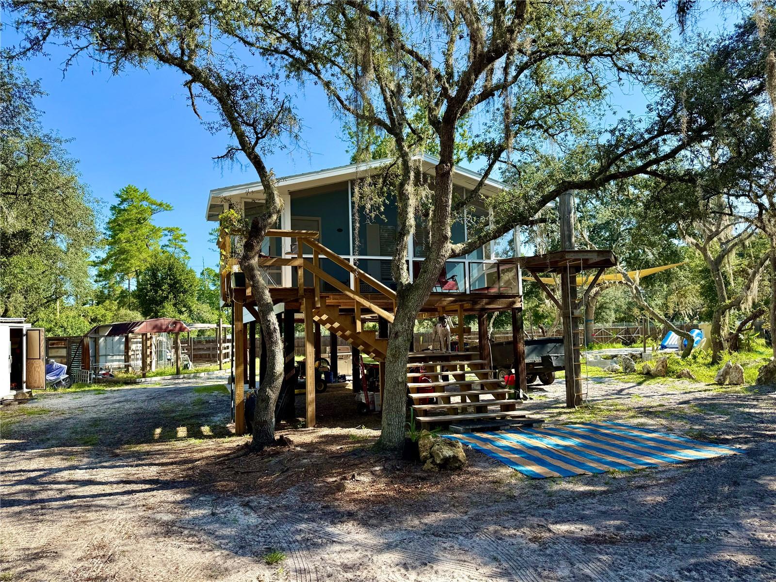 Are you searching for peace, quiet, and a personal retreat to call home — or perhaps the ultimate vacation getaway? This truly one-of-a-kind 1.24-acre paradise offers you that rare opportunity. Tucked deep in the heart of the forest, this property comes with more than just land and structures — it comes with a lifestyle. Featuring a 1-bedroom, 1-bathroom stilt home with a brand-new roof in 2025, a 2-bedroom, 2-bathroom 1985 manufactured home currently used as storage and laundry, and a 2-bedroom, 1-bathroom 2007 30’ Puma RV. Let’s start with getting there: the seller will meet you at the corner of SE 207th Terrace and SE 182nd Ave Rd. to personally guide you in. Trust us — you’ll want to follow him. Once you pass the "Game of Thrones" style automated gate flanked with citronella torches, you’ll know you’ve arrived. The entire property is fully fenced, with 3"–5" of under-fencing for added security. As you enter, the stilt home stands proudly ahead, showcasing its brand-new grand staircase leading to a screened-in front porch. The property boasts 200-amp electrical service with two separate meters — a 100-amp service at the manufactured home — and features 2 RV hookups with 50-amp power and 4 sewer connection points. Inside the stilt home, you’ll find real wood floors, a tankless electric water heater, dual A/C units and heaters, keyless front entry, GFCI safety receptacles throughout, and the central hub for 8 Smonet security cameras and the property-wide Wi-Fi system. That same high-speed internet powers music, lights, a hi-end projector, and even the waterfall at the pond. Fiber optics have already been run and are expected to be connected soon. Exit the stilt home and ascend the "crane’s roost" to zipline down to your own private 4-foot-deep koi pond and 750,000 lbs of imported white sand beach. The pond is spring-fed, filtered, and crystal clear — ideal for swimming or just relaxing beneath the waterfall. It even serves as a water source for fire control, with a 2' firehose located in the well house. The koi (30–35 of them!) help keep the water naturally clean and don’t mind sharing the space with swimmers. Trust us — both the photographer and the listing agent took a dip! Head over to the Argentinian-style wood-fired grill and cook up a ribeye with real oak logs — just like the seller did during our visit, complete with sweet corn roasted in-husk right in the flames. The property runs on well water and includes an iron eater system with two carbon filters and one resin filter. Need space for your hobbies or farm life? There’s a concrete-floored chicken coop, two horse stalls, an automated back gate with a concrete footer (wiring in place, just needs connecting), and an unfinished meat-processing station ready for concrete — the water and drain lines are already in. An outdoor bathroom area adds more charm with a working toilet, dual shower heads, and a pebble floor lit by waterproof LED lighting. Forgot your soap? No problem — there’s even a soap plant growing right inside the shower. Whether you're riding out from the back gate on horseback, exploring the land on an ATV, or preparing for a day of outdoor adventure, this property delivers. Watch everything come to life on video at https://youtu.be/zTCFfv3849w. Call today for your private tour and step into a lifestyle that combines off-grid serenity with modern luxury in a way you truly have to see to believe.
