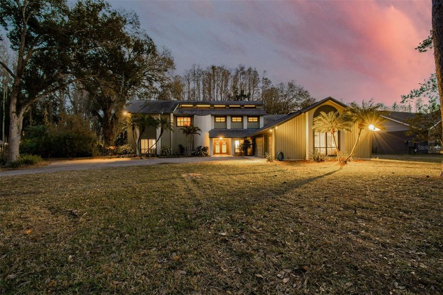 Gracefully positioned along the water and privately set on over 1.14 acres of picturesque grounds, this exceptional lakefront residence offers 5 bedrooms, 3.5 baths, an oversized three car garage, and a resort-style pool. Surrounded by sprawling pine trees and tranquil views, the setting evokes a sense of serenity and retreat rarely found in residential living. Inside, the home is defined by soaring vaulted ceilings, dramatic architectural lines, and abundant natural light, creating a feeling of openness and warmth. Elegant plantation-style shutters throughout add timeless character and refinement. The gourmet kitchen serves as a stunning focal point, beautifully positioned to capture views of the pool, grounds, and lake beyond. Anchored by a spacious center island and enhanced by custom cabinetry, refined lighting, and a beautifully integrated designer range hood, the space blends function and design effortlessly. Overhead and under-cabinet lighting create a warm ambiance, while the premium appliance package includes a dishwasher, new cooktop stove, built-in oven, refrigerator, microwave, wine fridge, and more. A whole house intercom system enhances convenience and connectivity. The family room offers an inviting gathering space centered around a beautiful wood burning fireplace, creating a warm and intimate atmosphere. The primary suite is a true private retreat with direct access to the pool and outdoor living areas. The primary bath offers a spa like experience, featuring dual vanities, a soothing jacuzzi tub, a walk-in shower with dual shower heads, custom cabinetry, beautiful lighting, and a private water closet. A remarkable custom closet system and dedicated AC further enhance comfort and luxury. The thoughtful layout includes two Jack and Jill bathrooms connecting secondary bedrooms on both levels, along with a convenient half bath downstairs. Each bathroom features a walk-in shower, blending modern design with everyday ease. An upstairs laundry chute adds additional convenience, while a built-in cigar humidor reflects distinctive custom detail. Outdoors, the property transforms into a private resort style escape. A sparkling pool with cascading spa and integrated hot tub, expansive screened pavilion, outdoor kitchen, BBQ area, and custom bar equipped with a five-keg cooler create an entertainer’s paradise. Commercial-grade cooking features, stainless steel prep areas, and an integrated surround sound speaker system elevate the experience. Sweeping lake views and breathtaking sunsets provide a spectacular backdrop. A private boardwalk leads to the owned dock, offering rare and highly sought-after lake access for kayaking, paddleboarding, gentle boating, and quiet reflection. Recent improvements, enhance peace of mind and overall livability. Newer roof, hot water heater, and iron removing water softener system, enhance both comfort and long term peace of mind. This is more than just a home. It is a lifestyle property defined by privacy, atmosphere, and refined lakefront living. Welcome home...