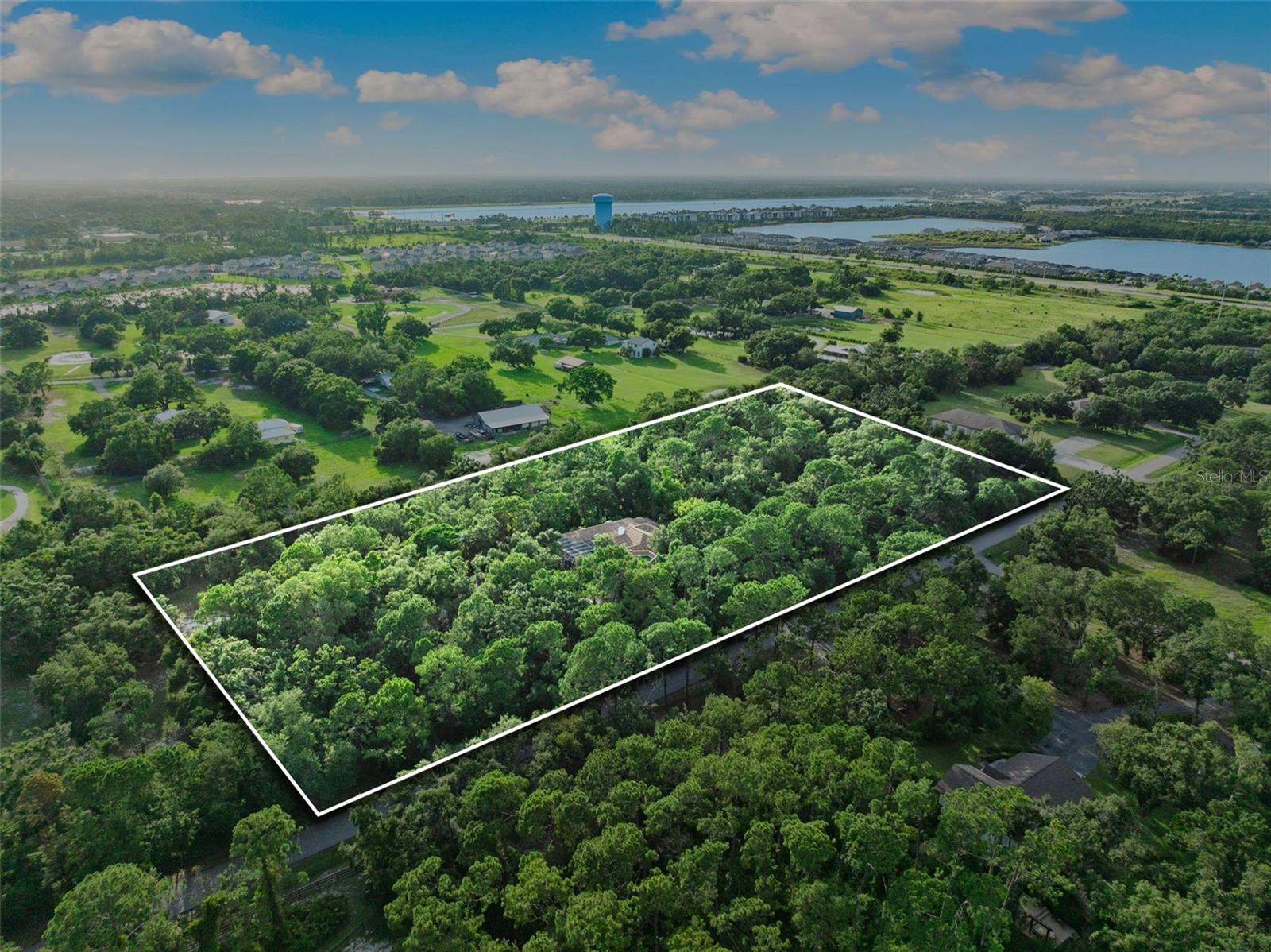 Welcome to the exclusive community of Pine Valley Ranches, where privacy and natural beauty converge on this stunning 5.5-acre estate. Tucked away among over 1000 exotic trees, foliage and lush landscaping, the property radiates the tranquility and botanical charm of a mini Selby Gardens. A double-gated entrance and winding paver driveway leads you through dappled sunlight beneath a majestic tree canopy, setting the tone for the serene lifestyle that awaits. With no neighbors in sight, privacy is absolute. (one can feel secure on this property) This custom-built Arthur Rutenberg residence spans approximately 7,000 total square feet with brand new roof and features 4 bedrooms, plus a den/office, and a remarkable three-story, Class 5 hurricane-rated safe structure—complete with a rooftop deck overlooking the verdant surroundings. Step inside through grand double doors into a spacious foyer that opens to a formal living area filled with natural light, 12-foot ceilings, and a skylight. A custom wet bar with a green onyx countertop and copper sink adds a touch of sophistication. Expansive double sliders open to a screened outdoor living area with a pool, area for grilling and oversized patio—ideal for entertaining. The triple-split floor plan offers privacy and functionality, enhanced by aquarium-style transom windows and octagon architectural accents. The expansive primary suite boasts two double sliders with direct access to the pool and outdoor lounge area. At the heart of the home, the recently renovated kitchen offers style and substance with custom wood ceiling insets, Samsung appliances, custom wood cabinetry, granite countertops, an extra-large pantry, and a large center island with comfortable seating for four. It flows seamlessly into a cozy family room with built-in shelving, an oversized marble fireplace, and a handcrafted wood mantle. The crown jewel of the property is the impressive three-story, Class 5 hurricane-rated addition. Designed with versatility in mind, it serves beautifully as a guest suite, art studio, man cave, or entertainment space. Constructed with double steel-reinforced concrete, fireproof and hurricane-rated windows, handcrafted walnut doors, this structure features floating maple floors, skip-trowel plaster walls and ceiling, custom lighting, and hand-painted cedar crown molding. A spiral staircase connects to a second-floor studio or workshop, while the third level offers a rooftop deck with artificial turf—perfect for sunbathing, sunset watching, or a roof top bar escape. Outdoors, immerse yourself in the peaceful surroundings. Meandering trails invite you through your private woods to explore the natural beauty of the property, which also features a koi pond and a detached concrete 400 sq ft garage—ideal for housing custom cars, tracker, golf carts, kayaks, paddleboards, and more. This unique estate is a nature lover’s dream, blending luxury living with the peace and serenity of a private botanical paradise. With its exceptional privacy and ample acreage, the property offers the opportunity to add a second residence. The opportunity is endless.