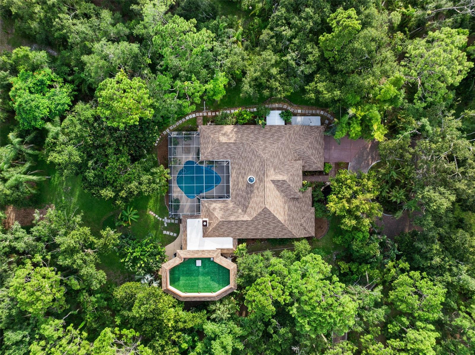 Welcome to the exclusive community of Pine Valley Ranches, where privacy and natural beauty converge on this stunning 5.5-acre estate. Tucked away among over 1000 exotic trees, foliage and lush landscaping, the property radiates the tranquility and botanical charm of a mini Selby Gardens. A double-gated entrance and winding paver driveway leads you through dappled sunlight beneath a majestic tree canopy, setting the tone for the serene lifestyle that awaits. With no neighbors in sight, privacy is absolute. (one can feel secure on this property) This custom-built Arthur Rutenberg residence spans approximately 7,000 total square feet with brand new roof and features 4 bedrooms, plus a den/office, and a remarkable three-story, Class 5 hurricane-rated safe structure—complete with a rooftop deck overlooking the verdant surroundings. Step inside through grand double doors into a spacious foyer that opens to a formal living area filled with natural light, 12-foot ceilings, and a skylight. A custom wet bar with a green onyx countertop and copper sink adds a touch of sophistication. Expansive double sliders open to a screened outdoor living area with a pool, area for grilling and oversized patio—ideal for entertaining. The triple-split floor plan offers privacy and functionality, enhanced by aquarium-style transom windows and octagon architectural accents. The expansive primary suite boasts two double sliders with direct access to the pool and outdoor lounge area. At the heart of the home, the recently renovated kitchen offers style and substance with custom wood ceiling insets, Samsung appliances, custom wood cabinetry, granite countertops, an extra-large pantry, and a large center island with comfortable seating for four. It flows seamlessly into a cozy family room with built-in shelving, an oversized marble fireplace, and a handcrafted wood mantle. The crown jewel of the property is the impressive three-story, Class 5 hurricane-rated addition. Designed with versatility in mind, it serves beautifully as a guest suite, art studio, man cave, or entertainment space. Constructed with double steel-reinforced concrete, fireproof and hurricane-rated windows, handcrafted walnut doors, this structure features floating maple floors, skip-trowel plaster walls and ceiling, custom lighting, and hand-painted cedar crown molding. A spiral staircase connects to a second-floor studio or workshop, while the third level offers a rooftop deck with artificial turf—perfect for sunbathing, sunset watching, or a roof top bar escape. Outdoors, immerse yourself in the peaceful surroundings. Meandering trails invite you through your private woods to explore the natural beauty of the property, which also features a koi pond and a detached concrete 400 sq ft garage—ideal for housing custom cars, tracker, golf carts, kayaks, paddleboards, and more. This unique estate is a nature lover’s dream, blending luxury living with the peace and serenity of a private botanical paradise. With its exceptional privacy and ample acreage, the property offers the opportunity to add a second residence. The opportunity is endless.